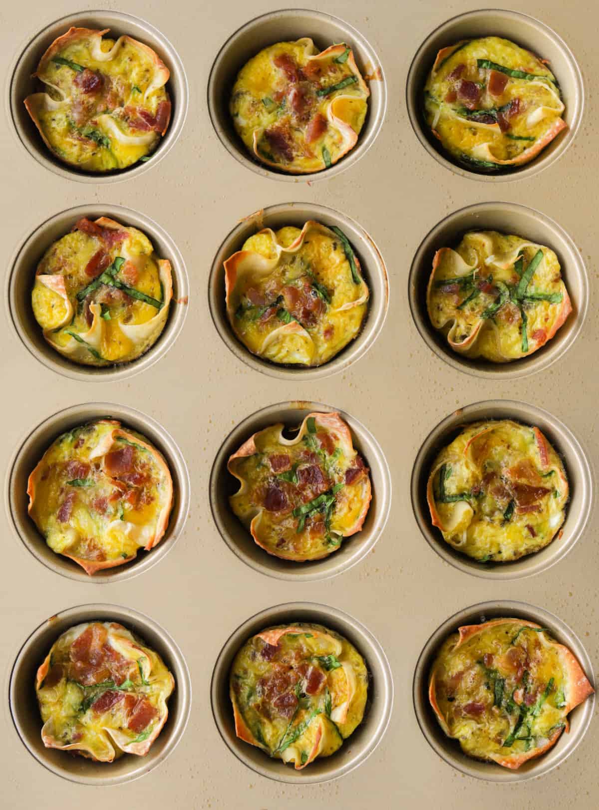 An overhead shot of cheesy wonton cups in a gold muffin tin.