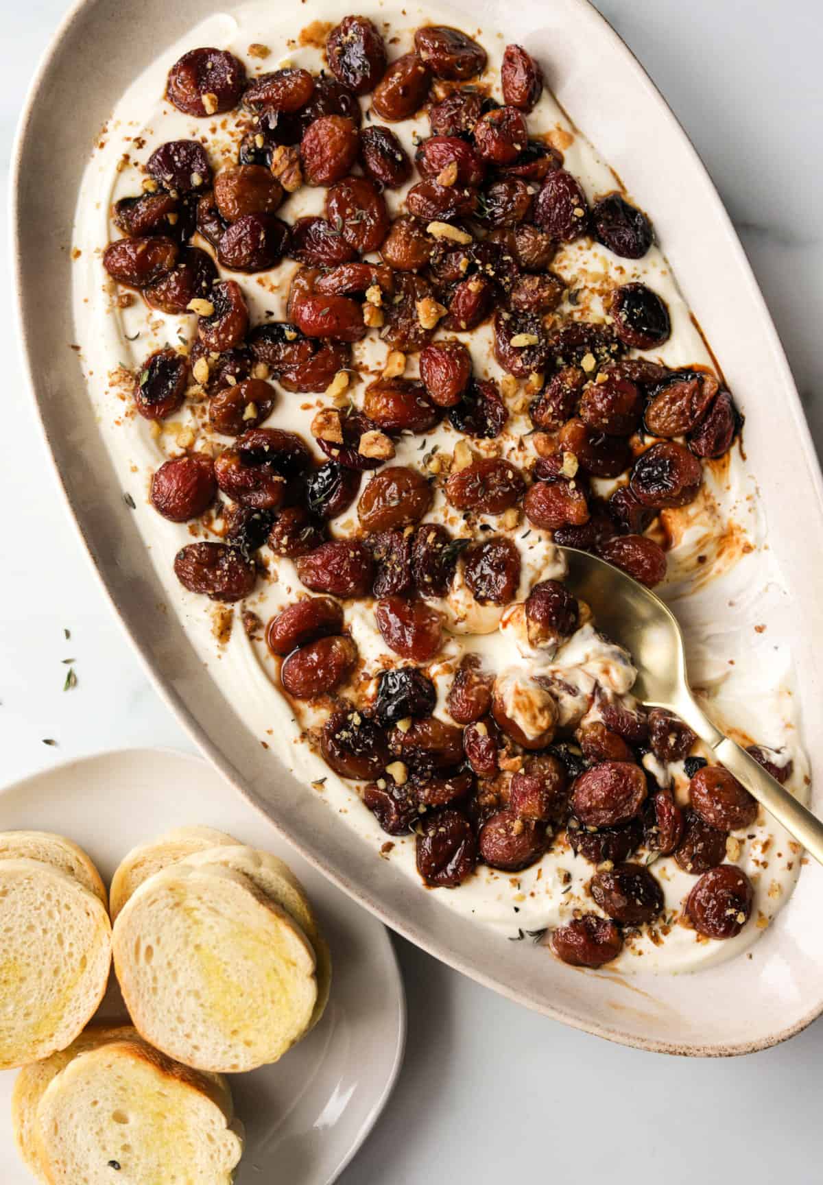 An overhead shot of ricotta dip with roasted grapes and a side plate of crostinis.