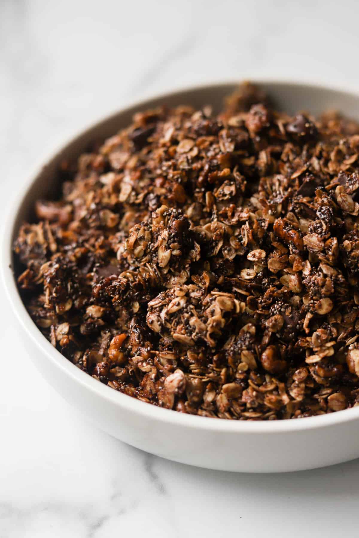 A side shot of a white bowl filled with dark chocolate granola.