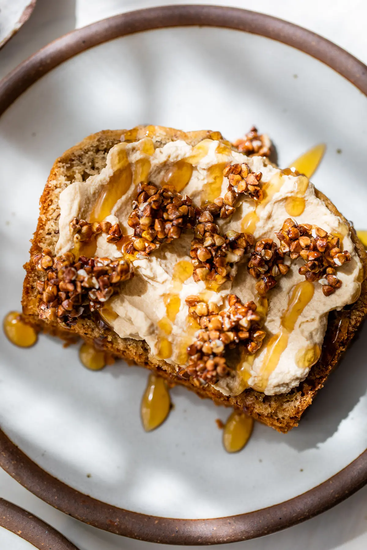 An overhead shot of a slice of banana bread with mascarpone and walnut clusters on top.