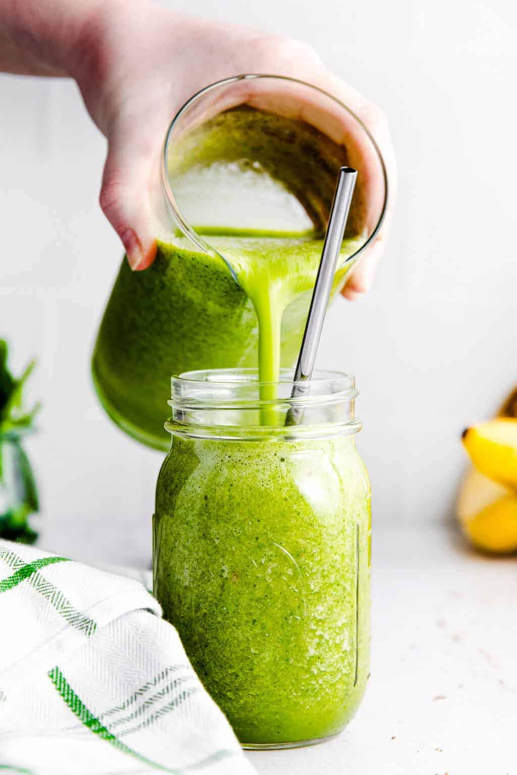 A side shot of a green smoothie being poured into a clear glass.