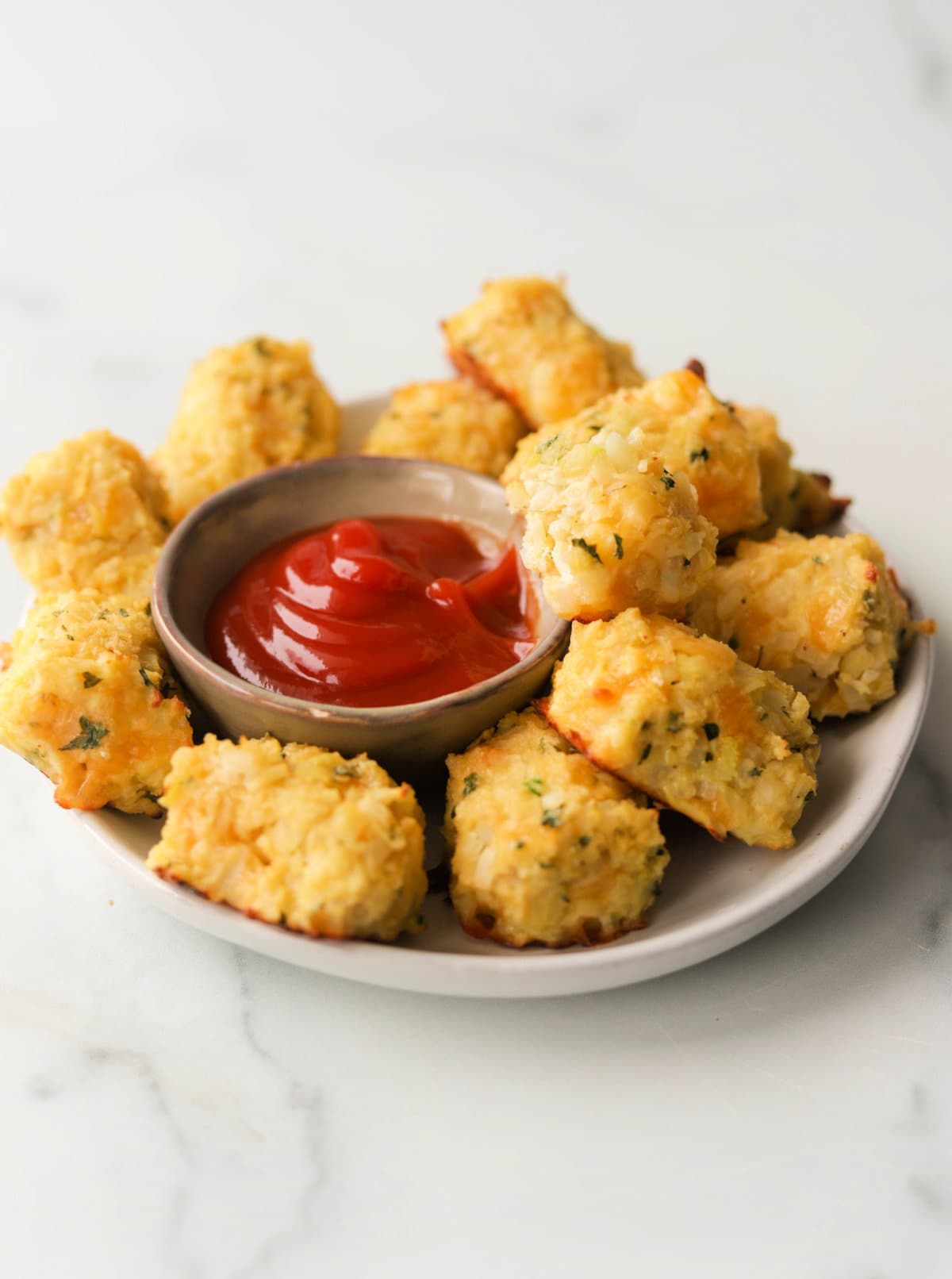 A front shot of a plate of cauliflower tater tots being dipped in ketchup.