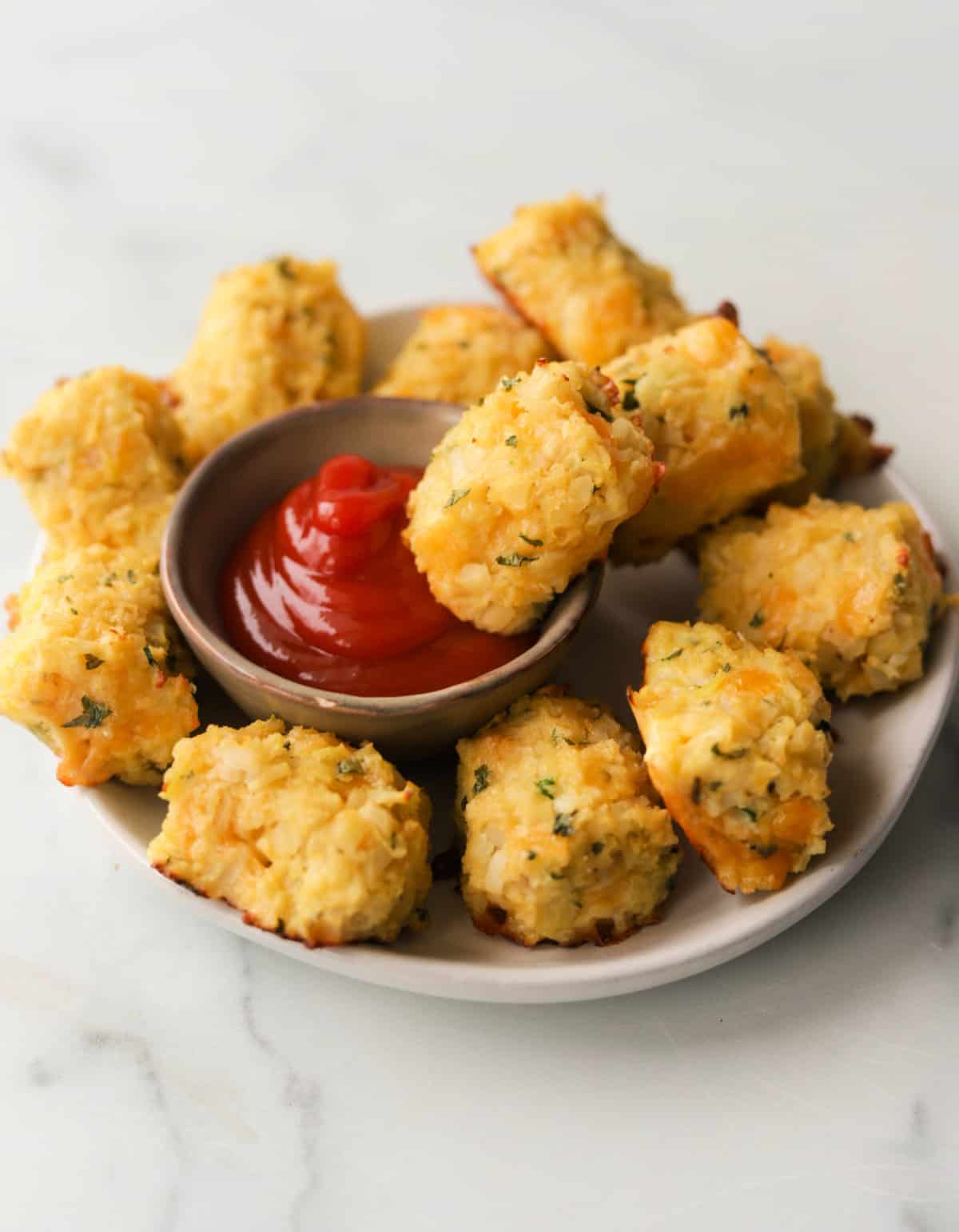A front shot of a plate of cauliflower tots with ketchup dipping sauce.