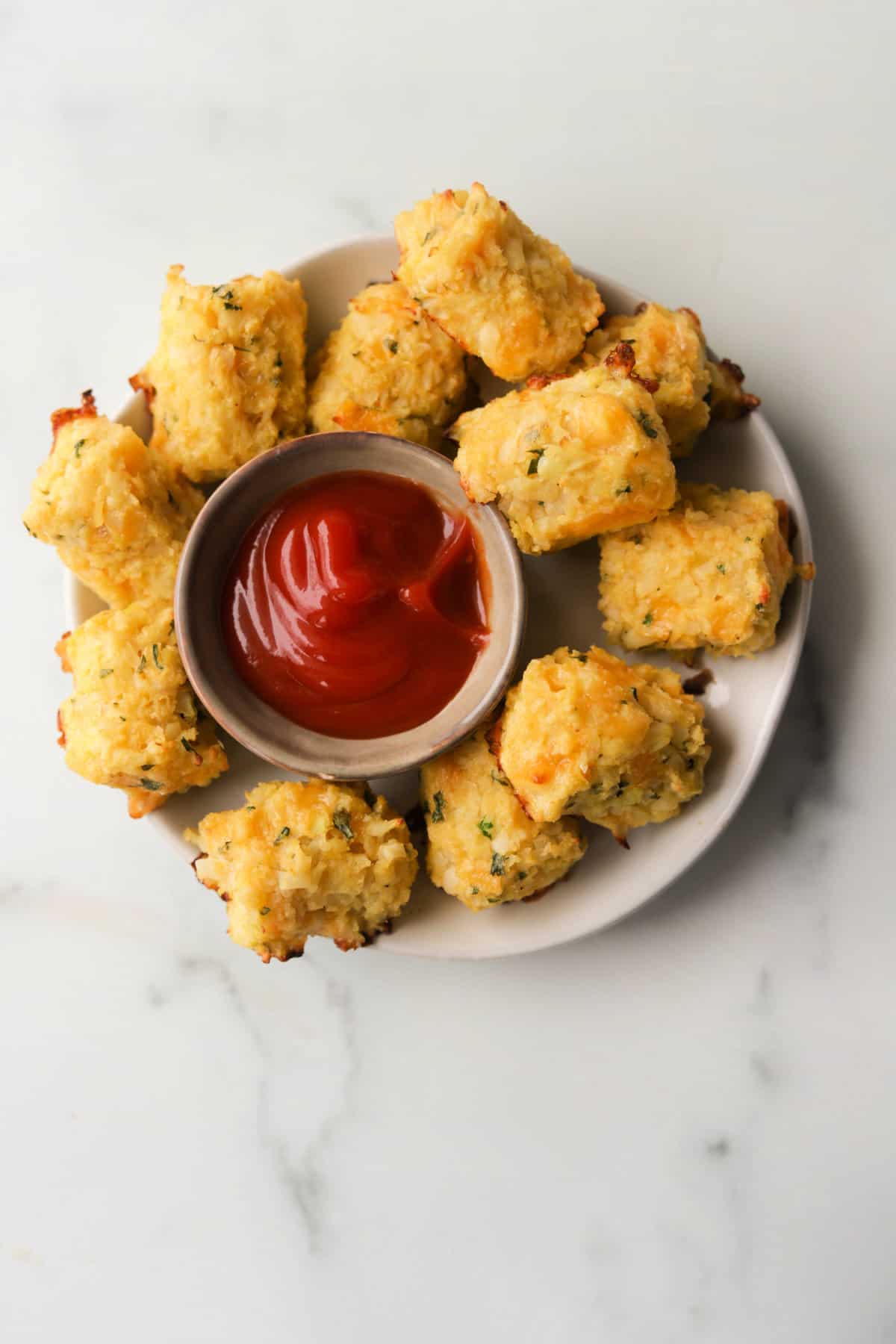 An overhead shot of a plate of cauliflower tots with ketchup for dipping.