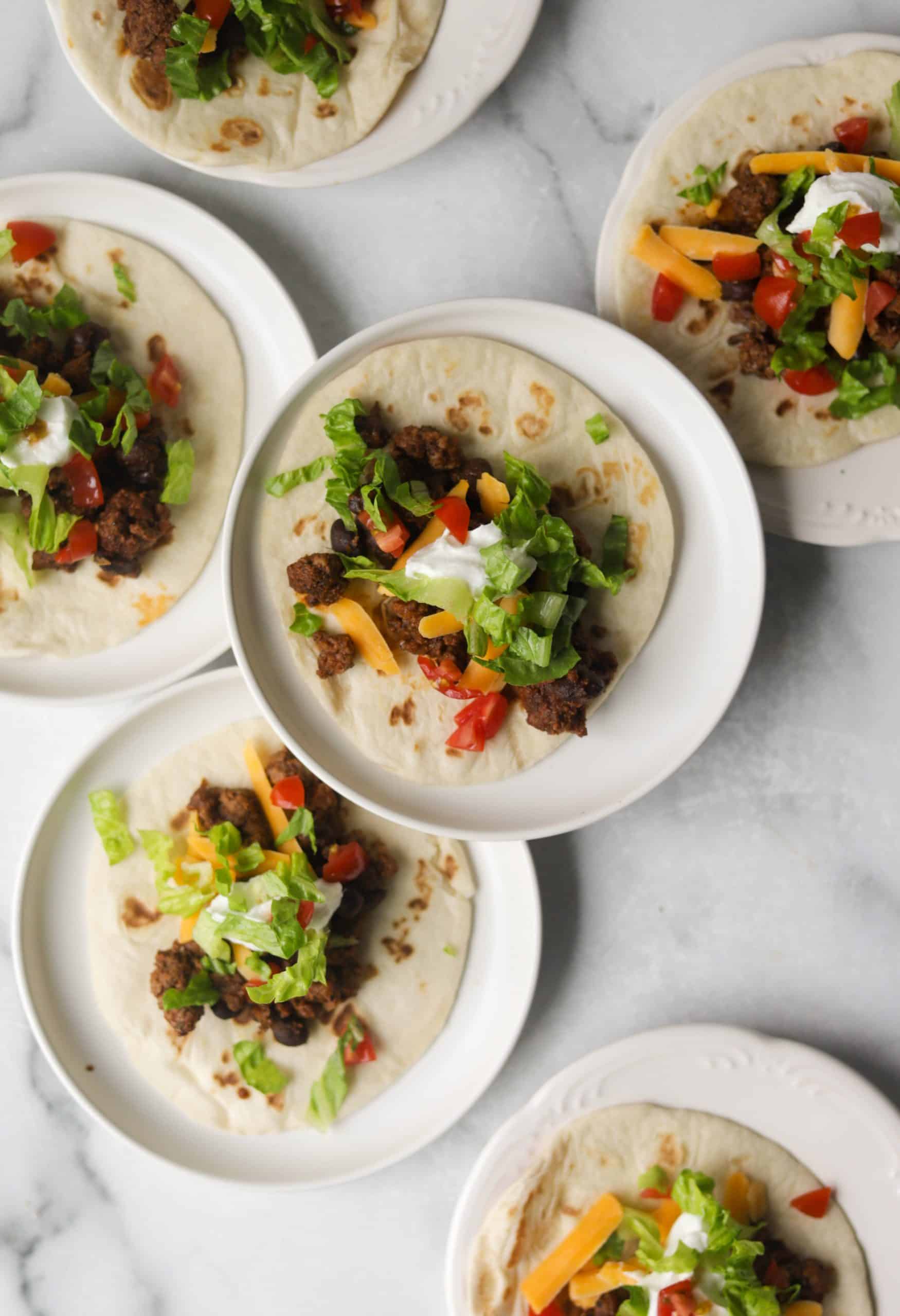 Several white plates with beef tacos on each.