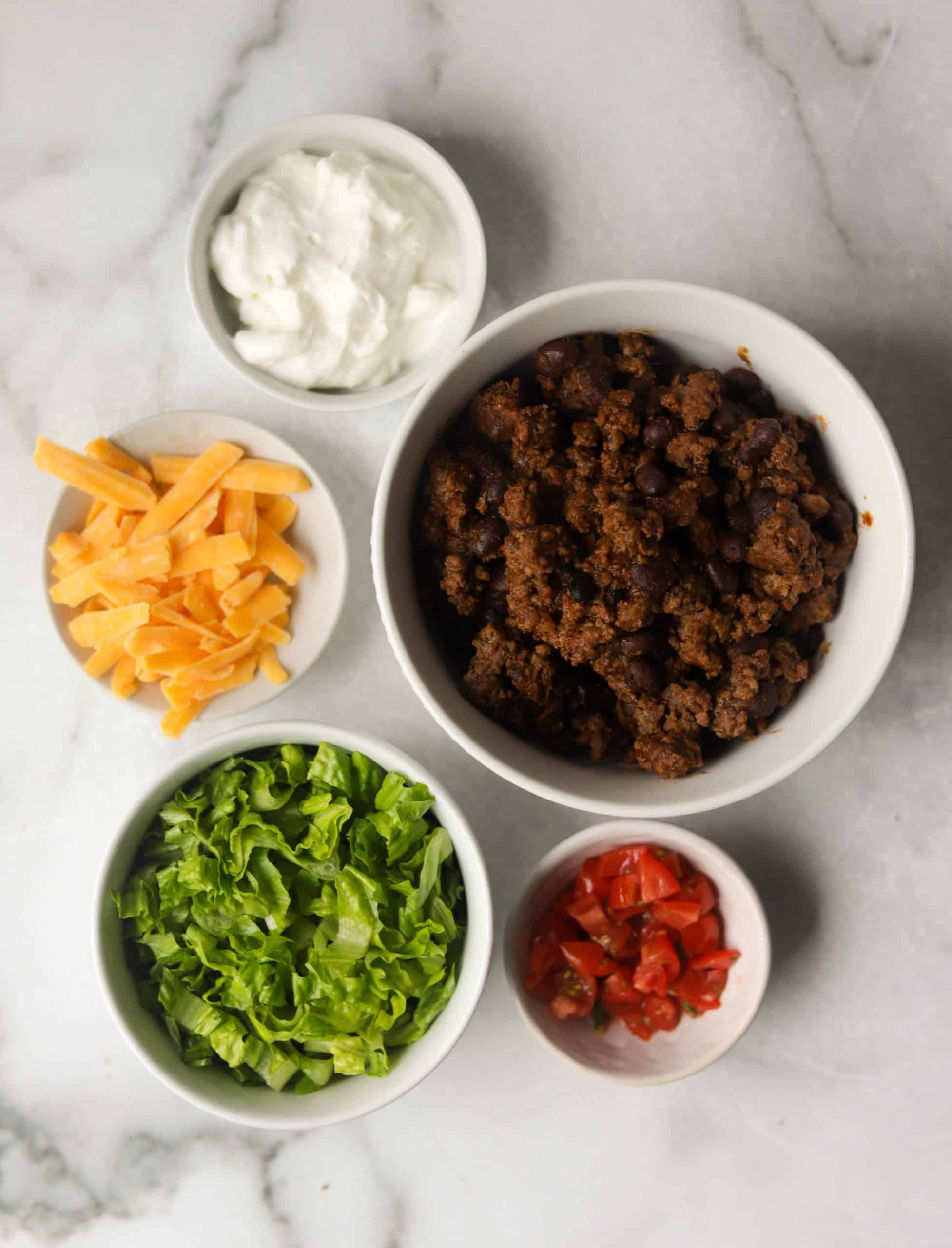 Several white bowls with taco ingredients in them.