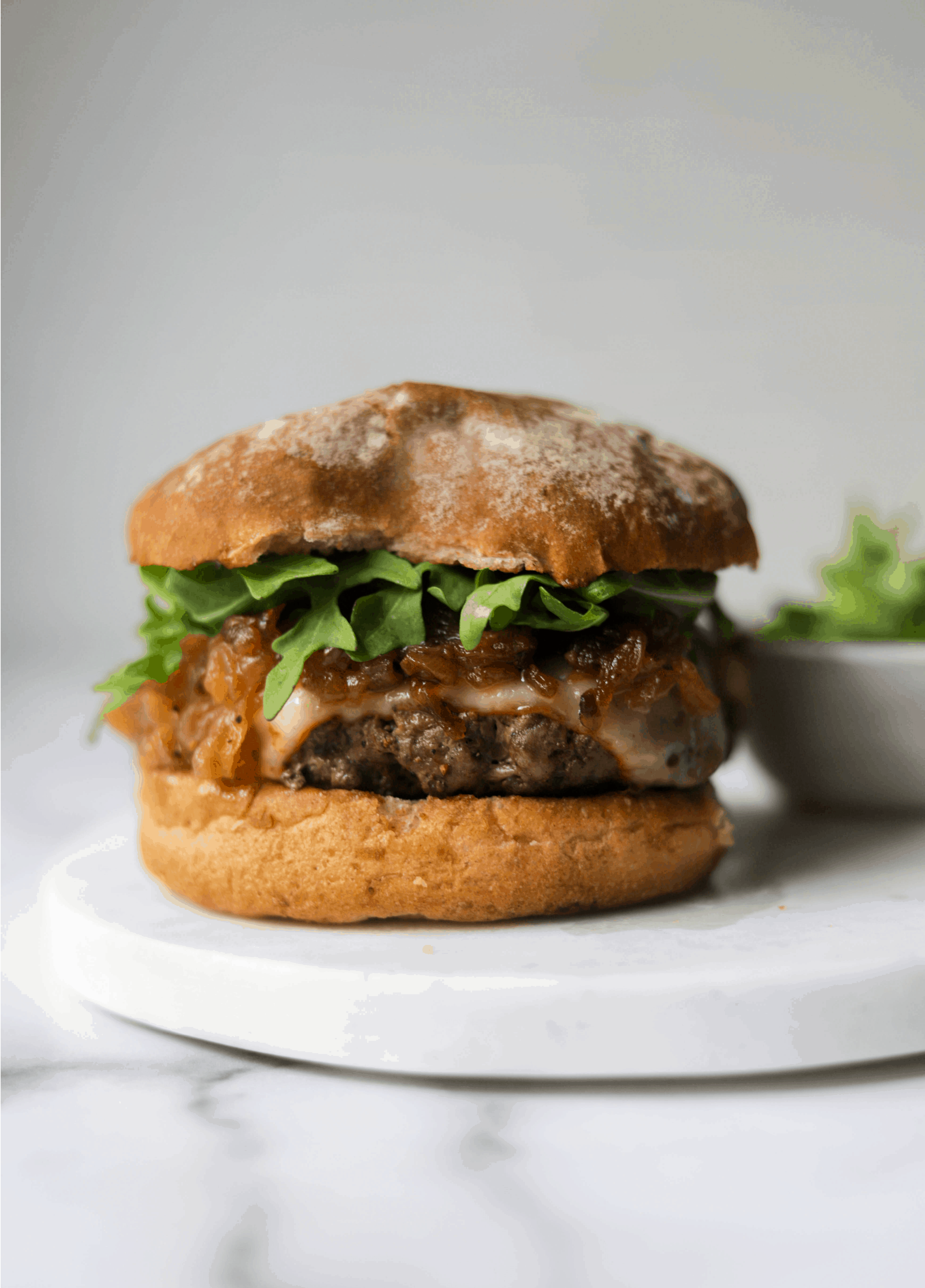 A burger with caramelized onions on a white marble platter.