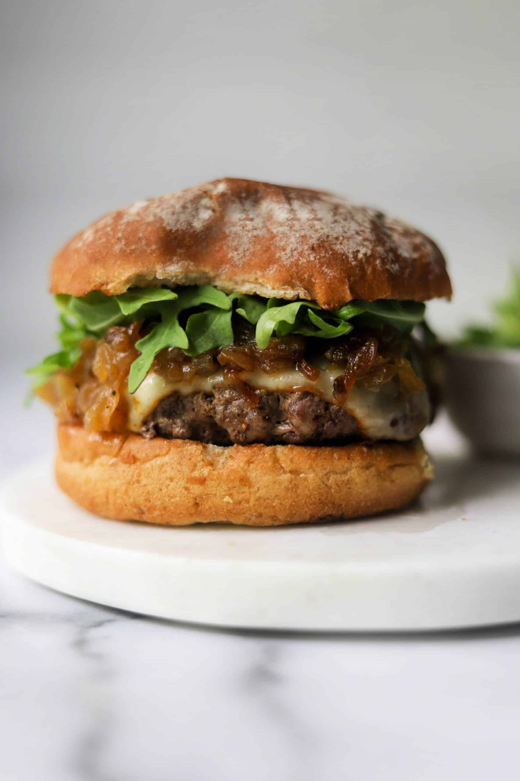 A caramelized onion burger with arugula on a white marble platter.
