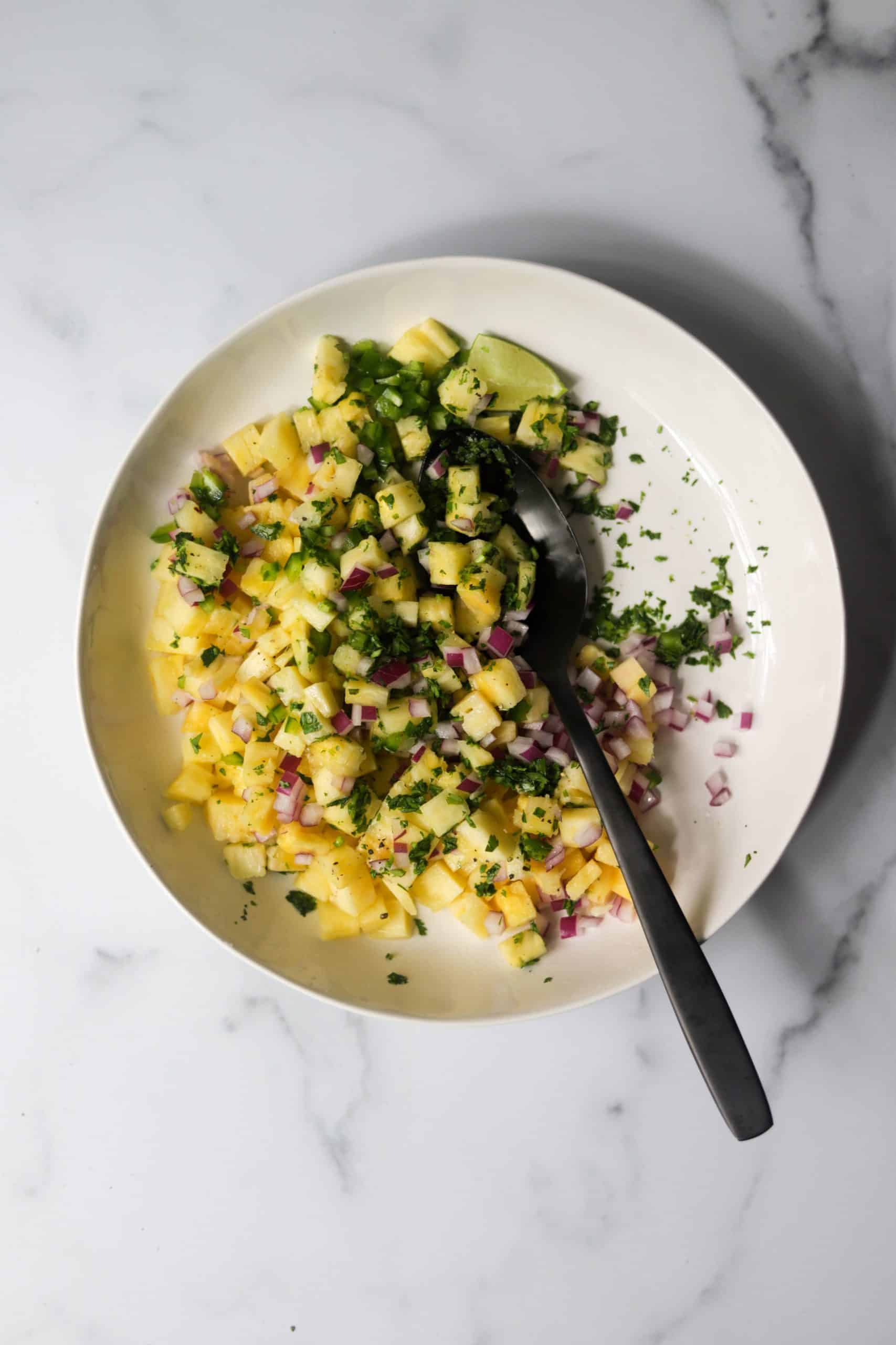 A white bowl with pineapple salsa with a black spoon.