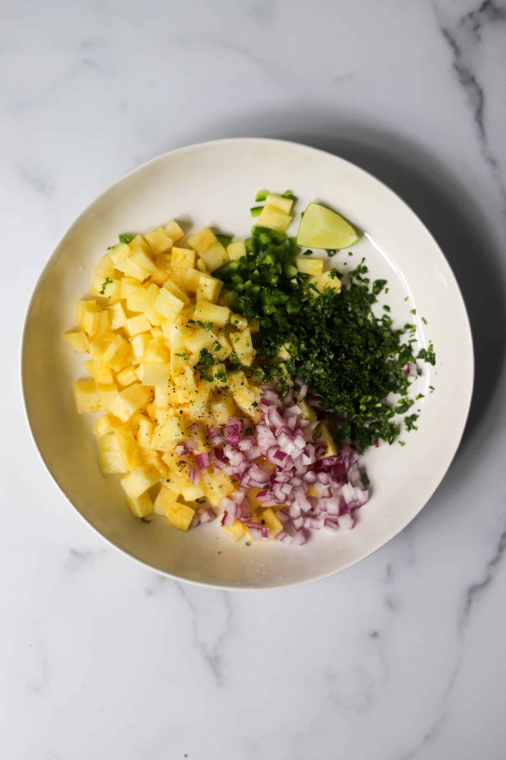 A white bowl with pineapple salsa ingredients.