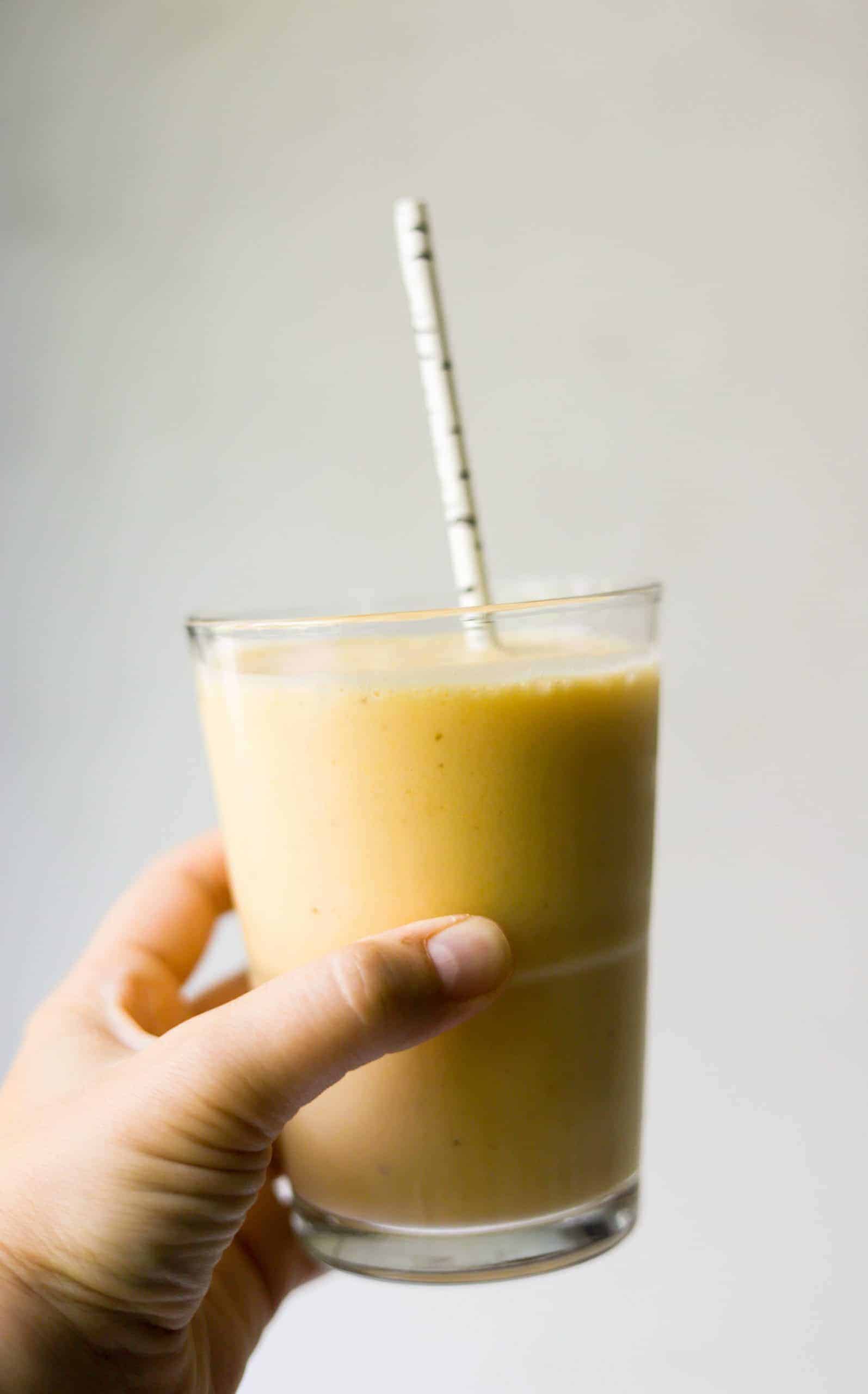 A hand holding a glass of banana peach smoothie.