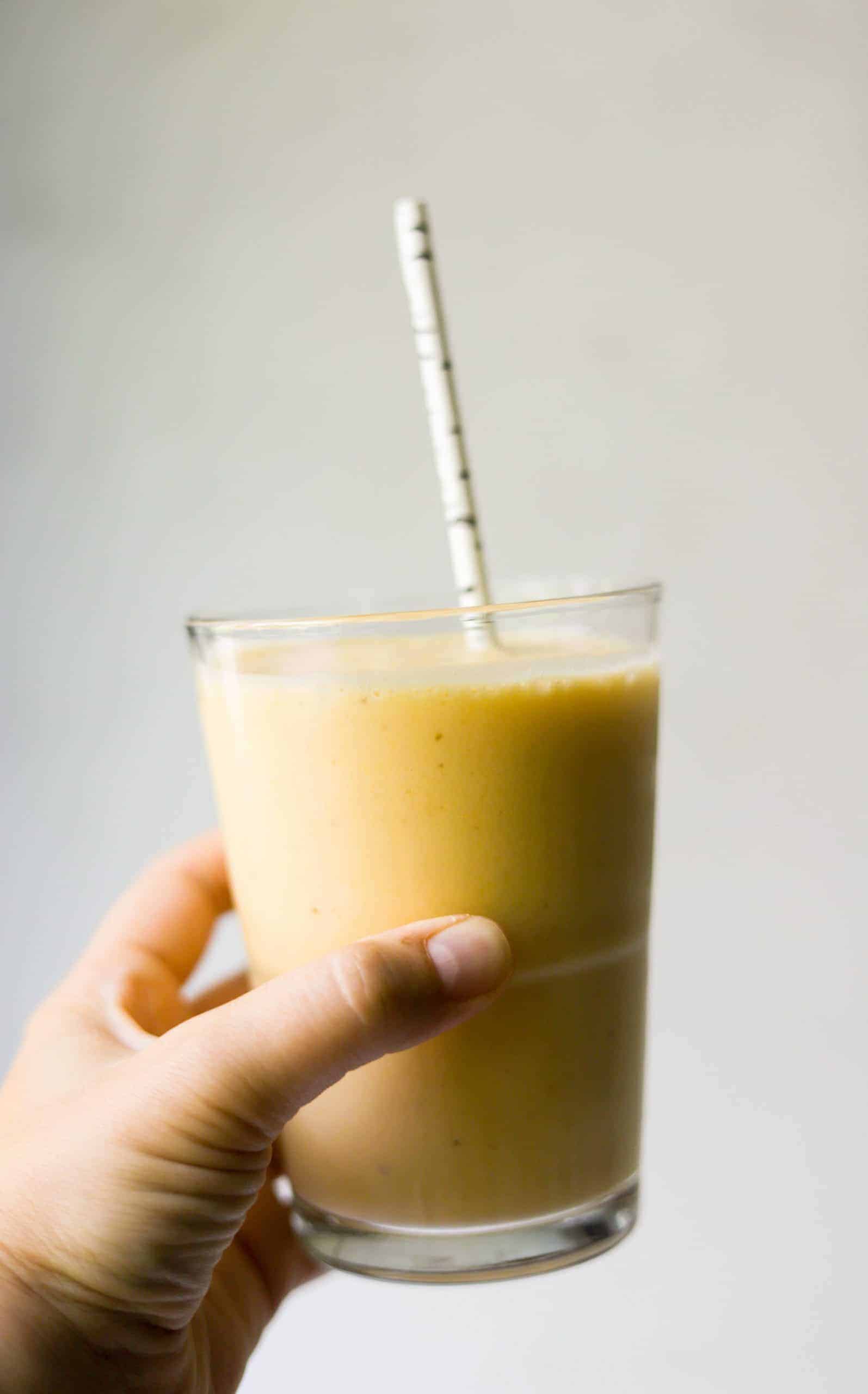 A side shot of a glass of a banana peach smoothie.