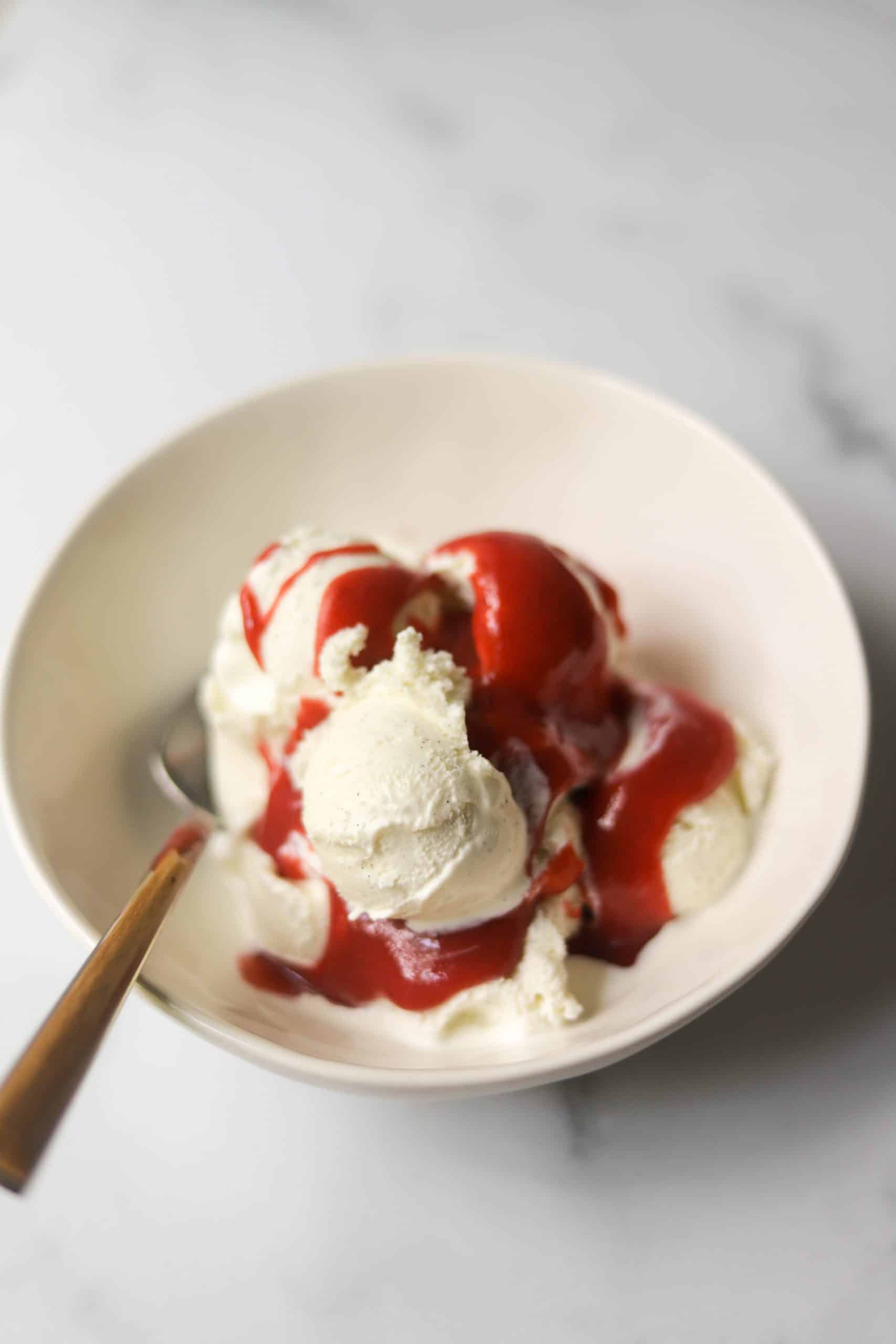 A white bowl with ice cream and strawberry syrup on top.