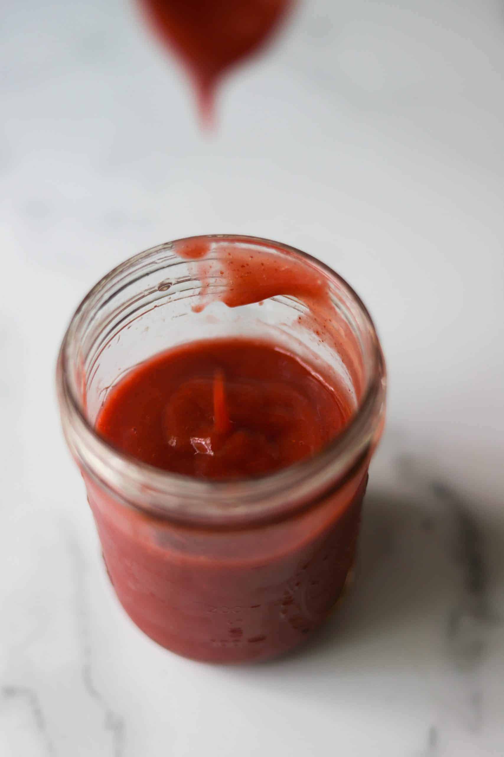 A clear jar with strawberry coulis.