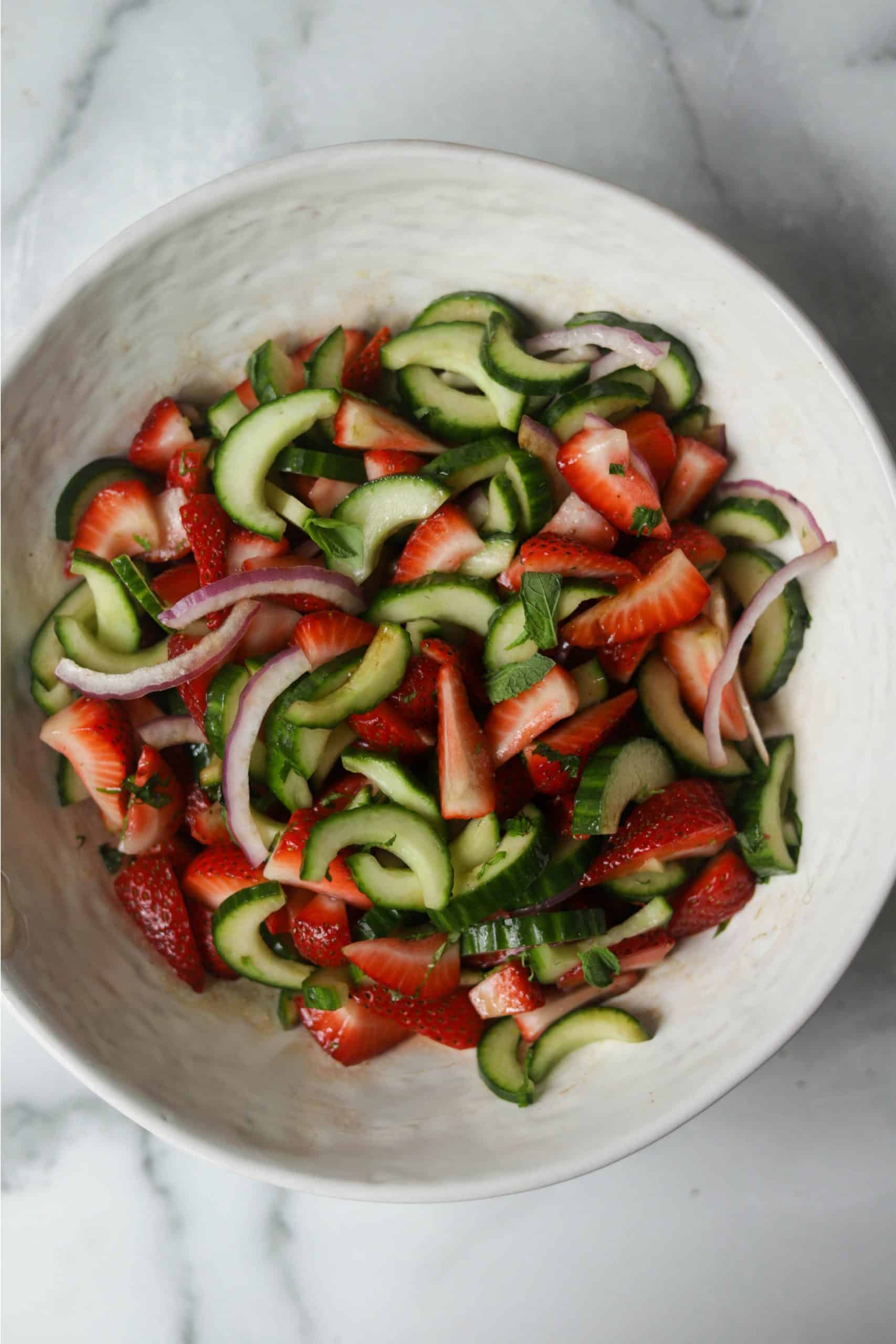 A white bowl filled with strawberry cucumber salad.