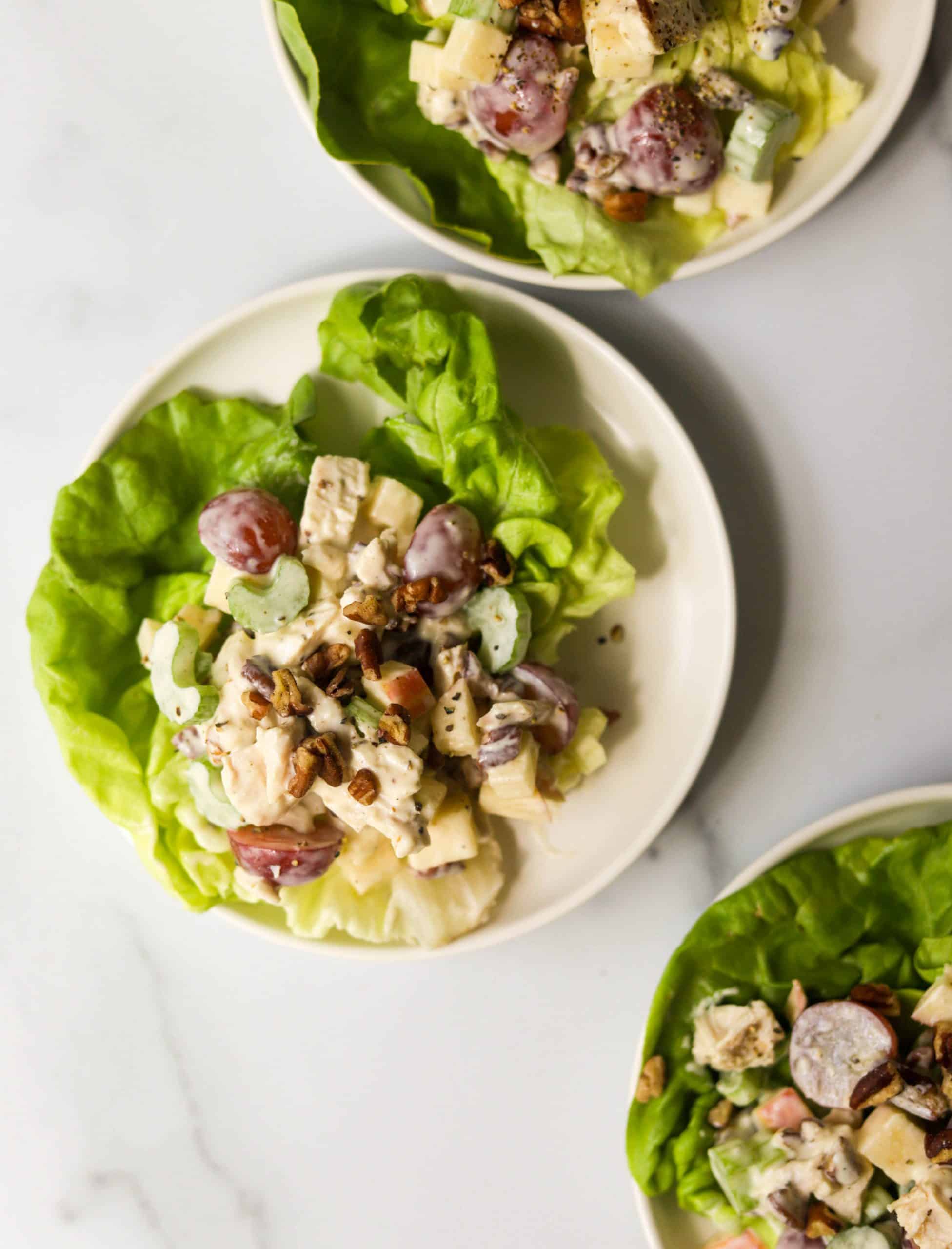 Three plates of apple walnut chicken salad on a marble white backdrop.