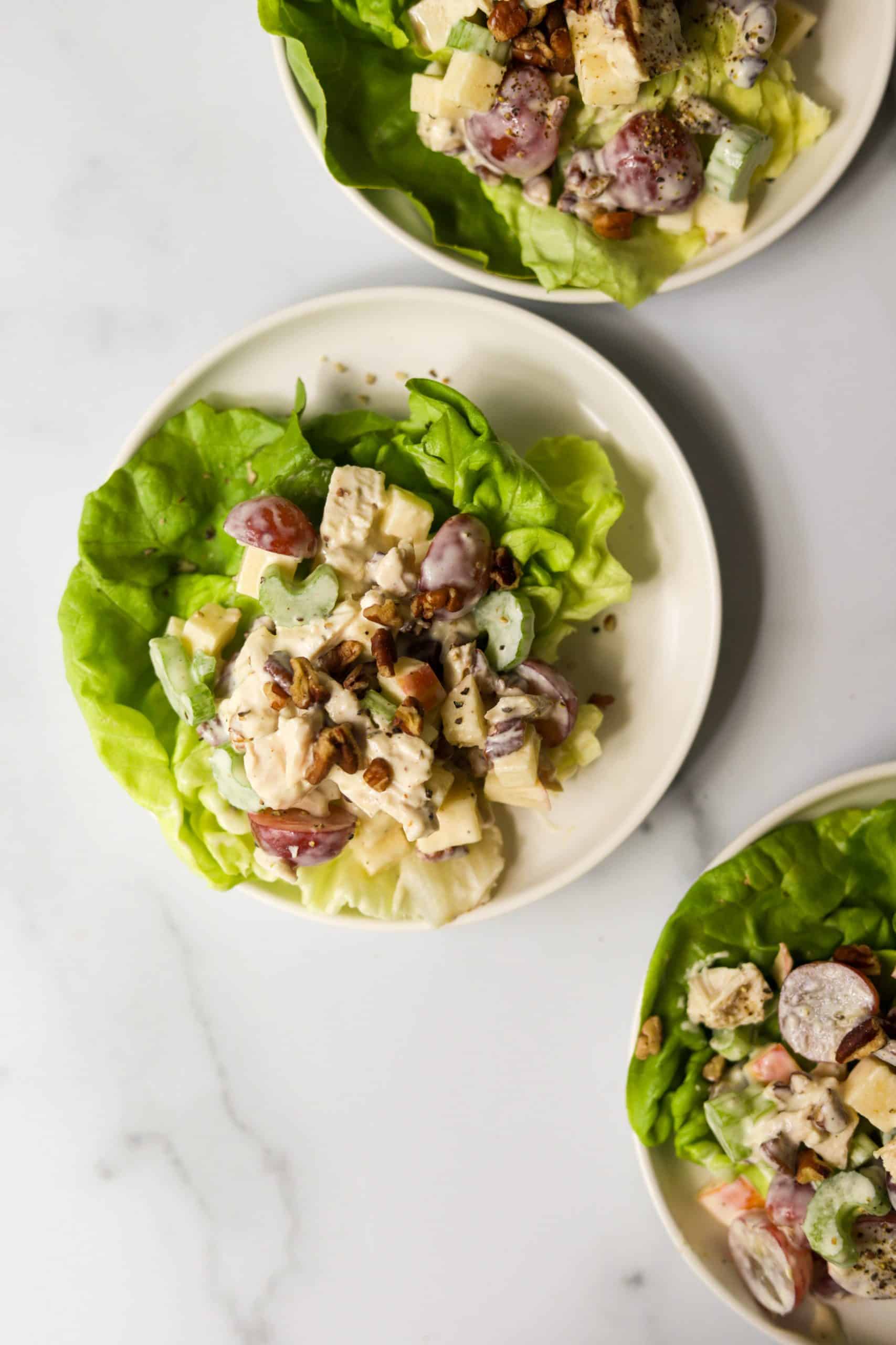 Three white plates with chicken salad on top on a white marble backdrop.