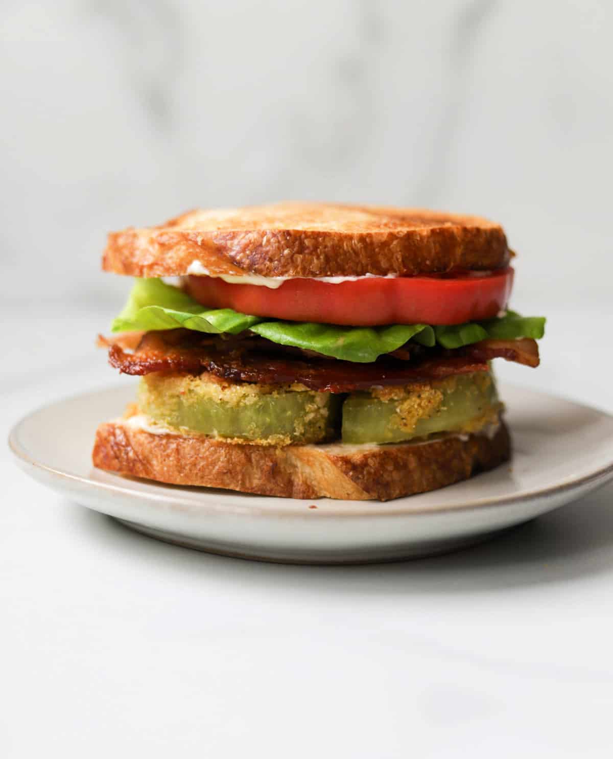 A front shot of a fried green tomato BLT on a white plate.