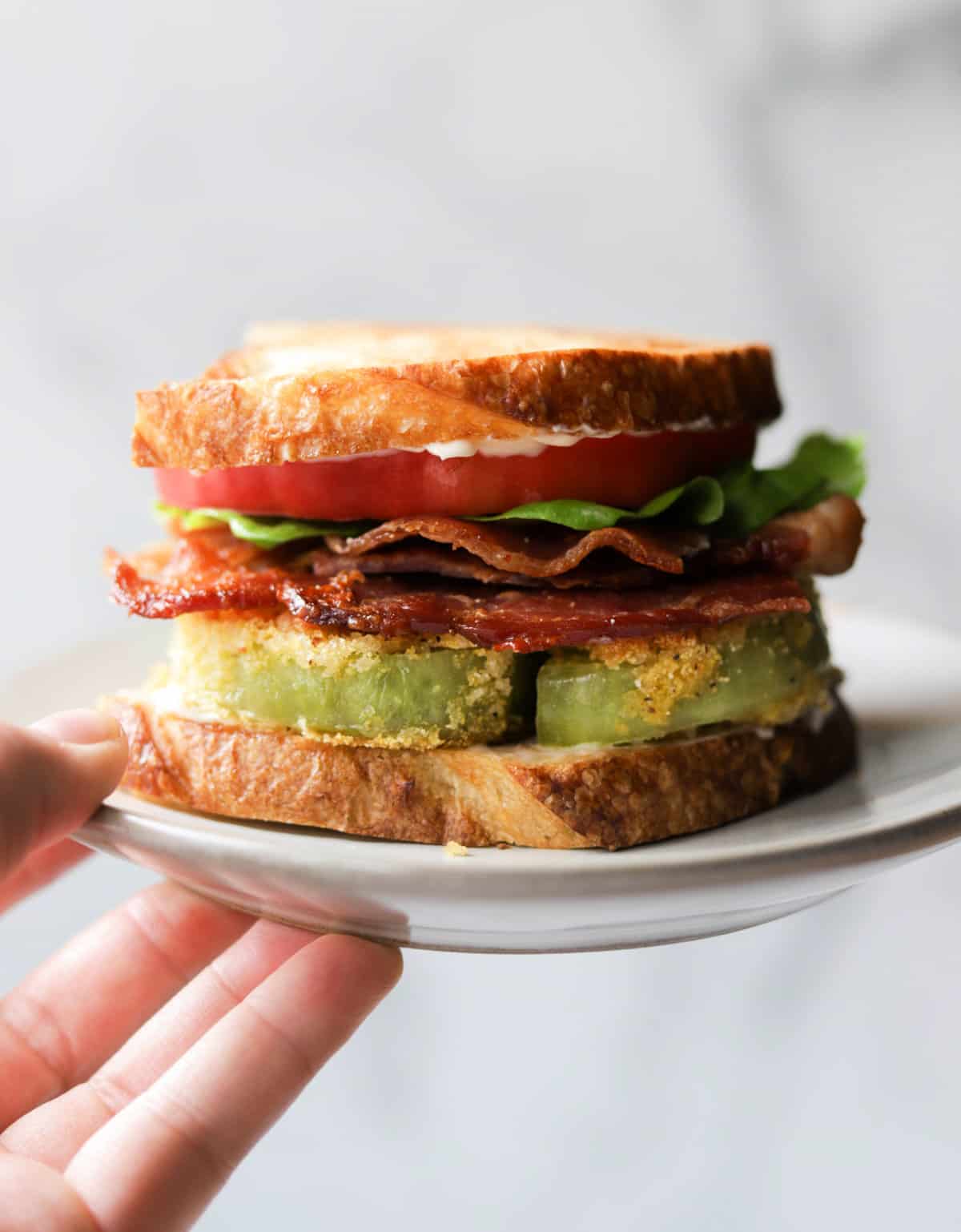 A front shot of a layered fried green tomato BLT on a white plate.