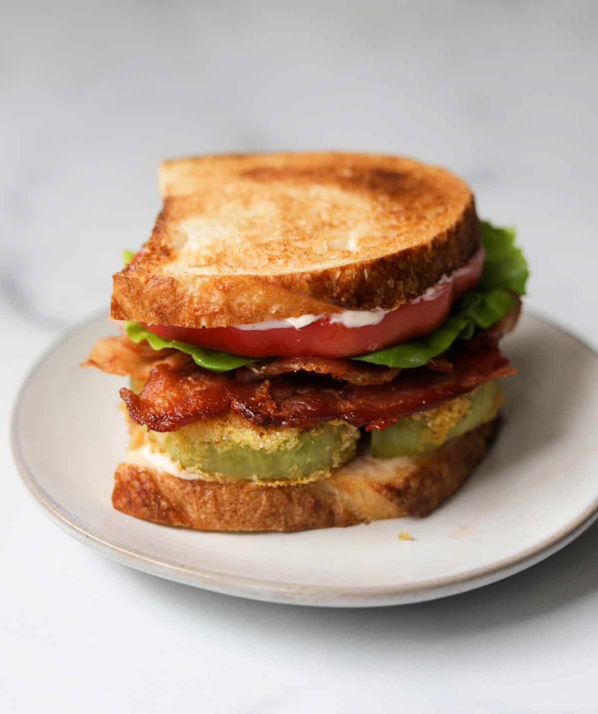 A side shot of a fried green tomato BLT on a white plate.