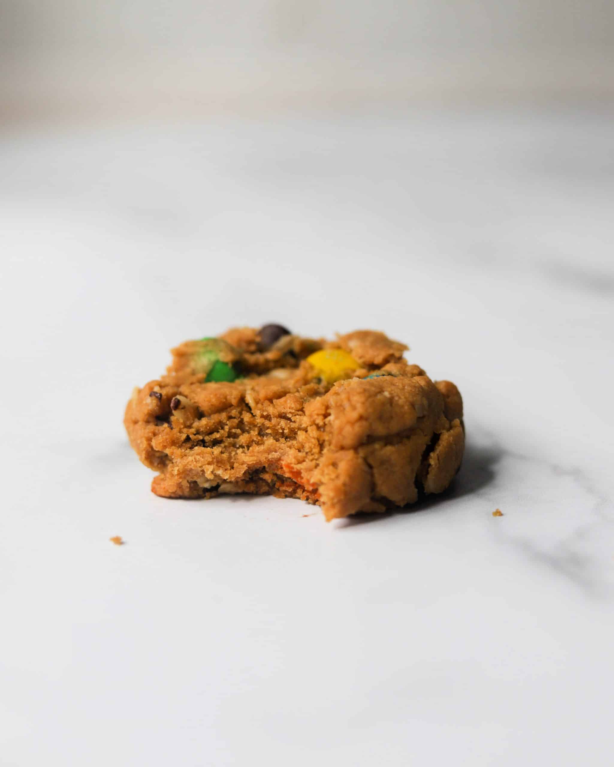 A single monster cookie on parchment paper with a bite missing.