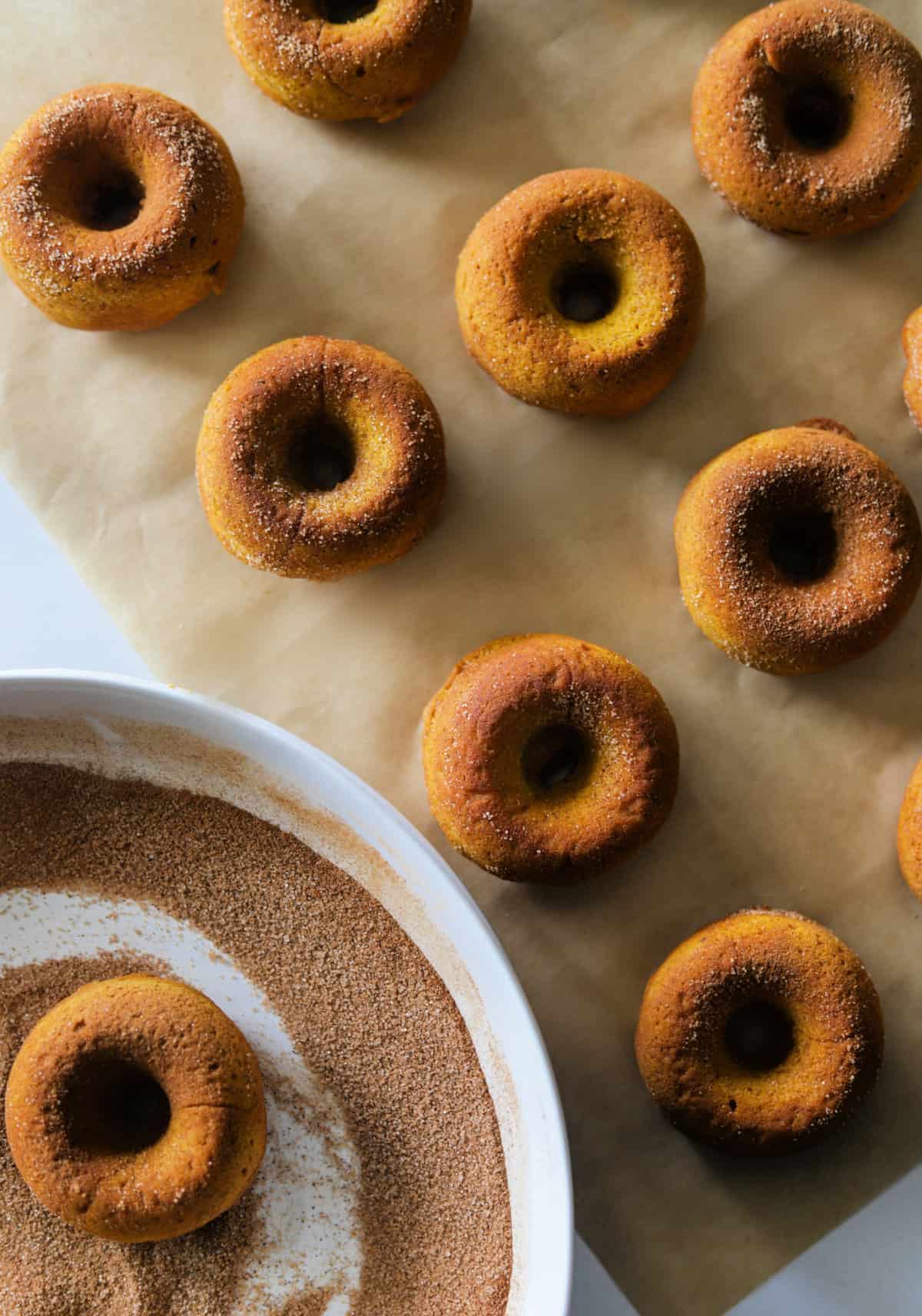 An overhead shot of pumpkin spice donuts lined on parchment paper with a dish on the side.