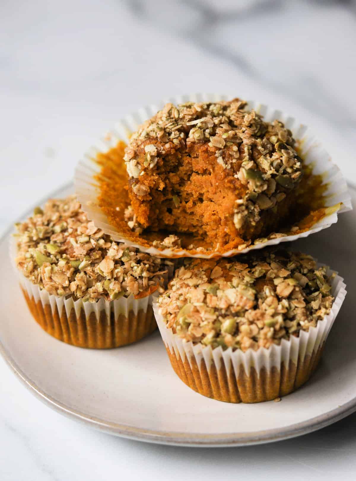 An angled shot of stacked oat flour pumpkin muffins with a bite taken out of the top one.