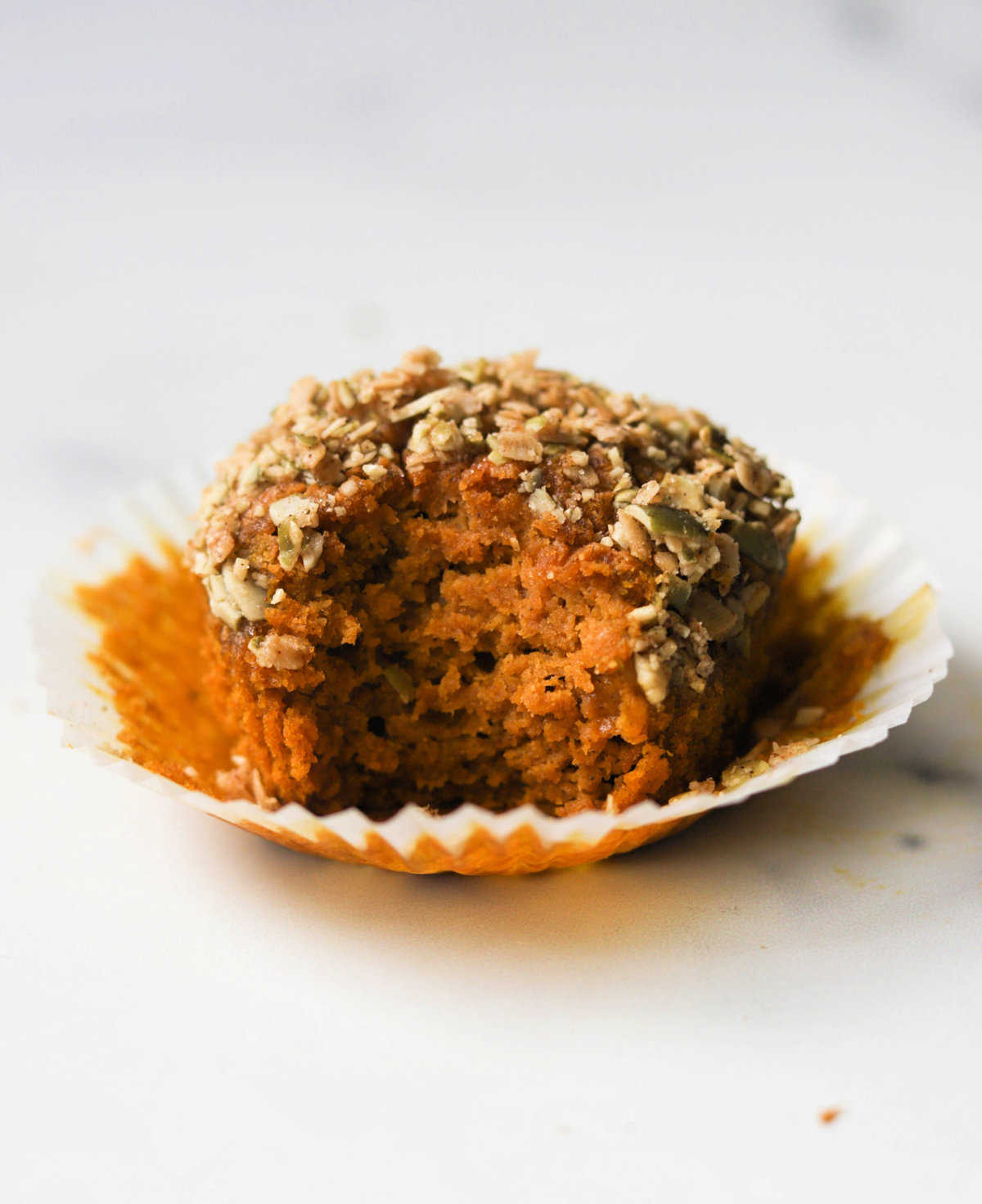 A front shot of a single oat flour pumpkin muffin with a bite taken out of it.
