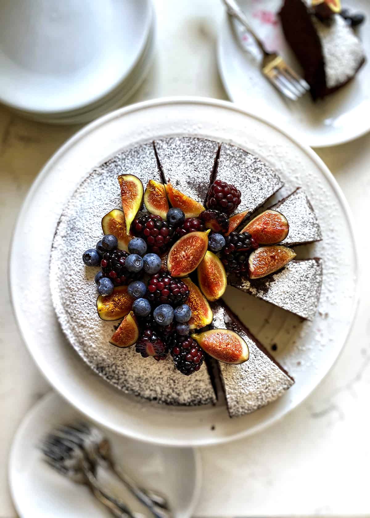 An overhead shot of chocolate olive oil cake with figs and berries on top.