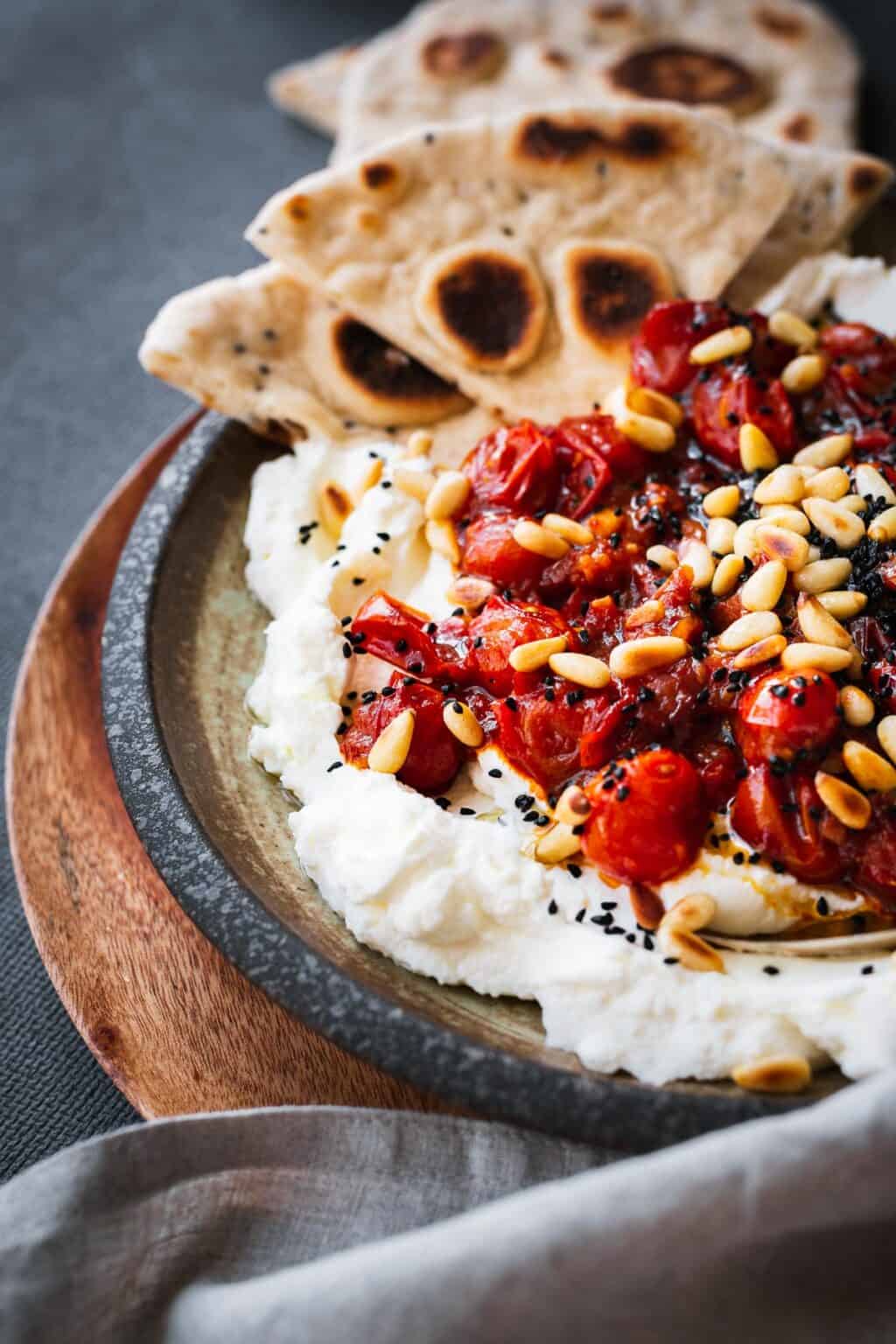 A side shot of labneh with roasted tomatoes in a dish.