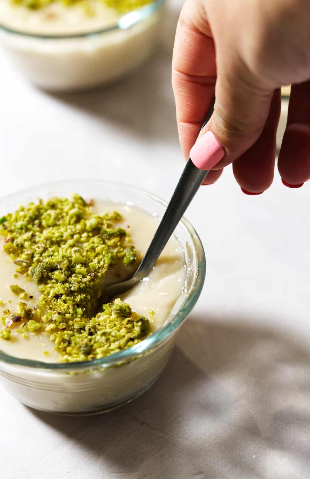 A side shot of a bowl of Lebanese rice pudding with pistachios on top.