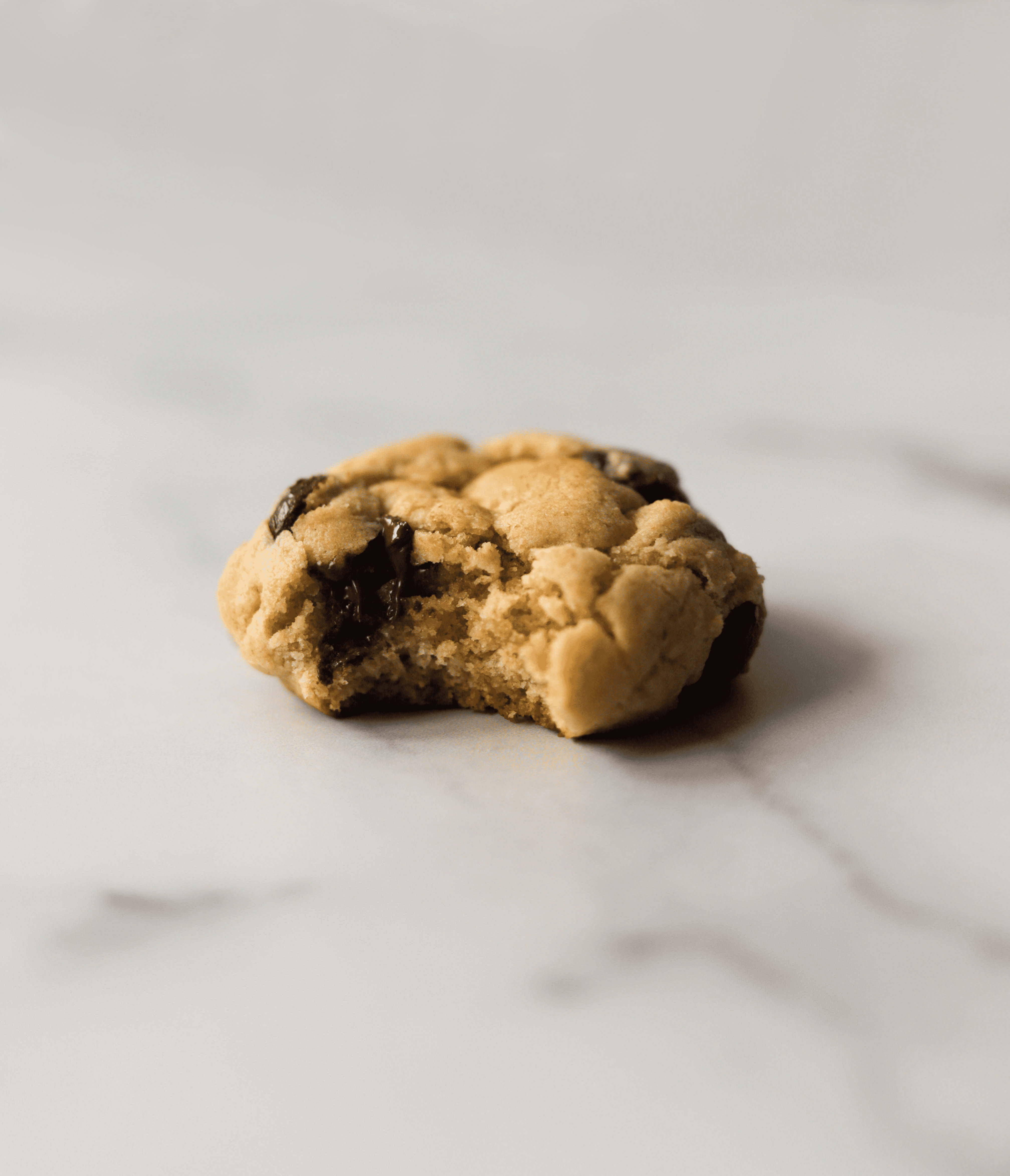 A side shot of a single miso chocolate chip cookie with a bite taken out of it.