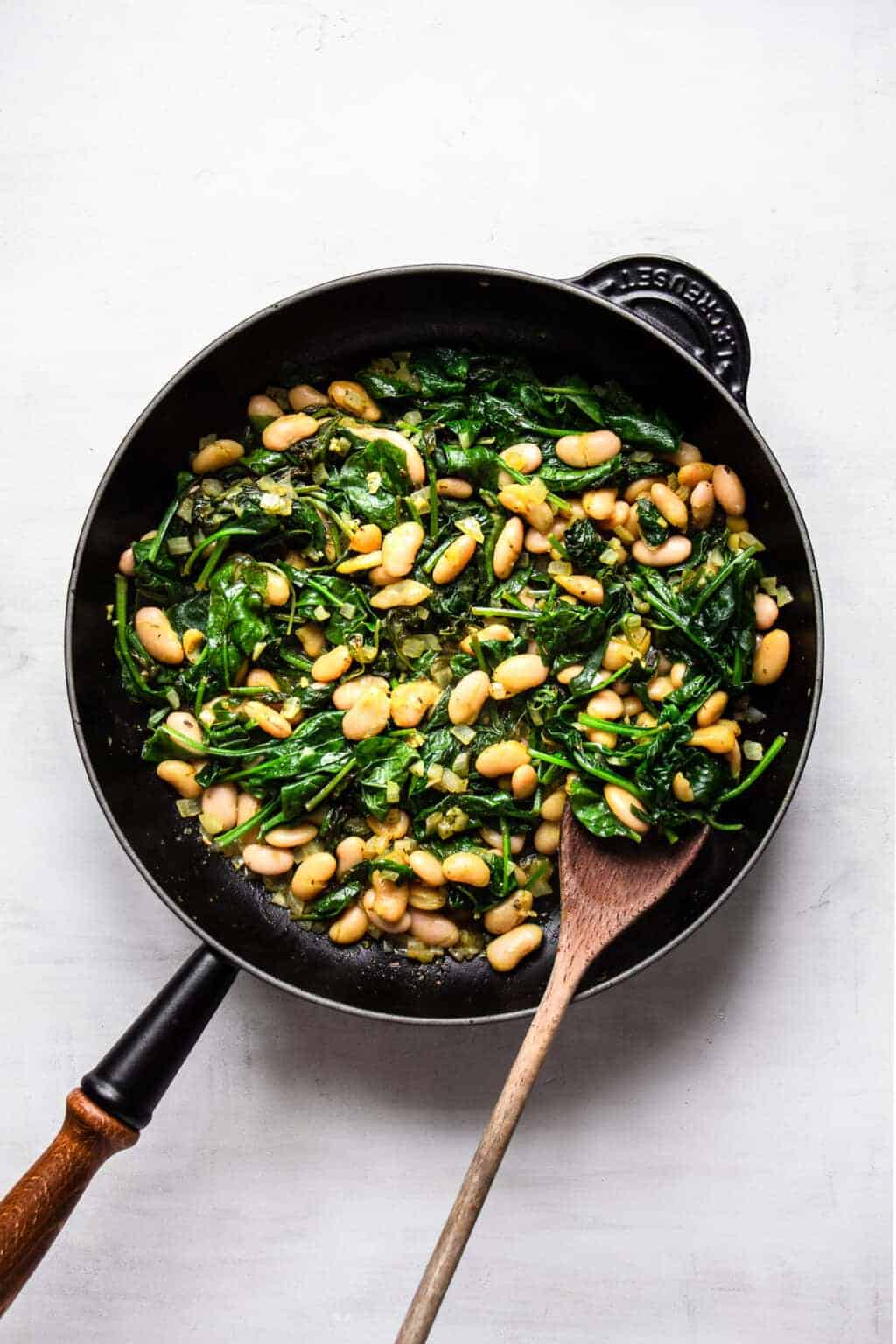 An overhead shot of a skillet of white beans and spinach.