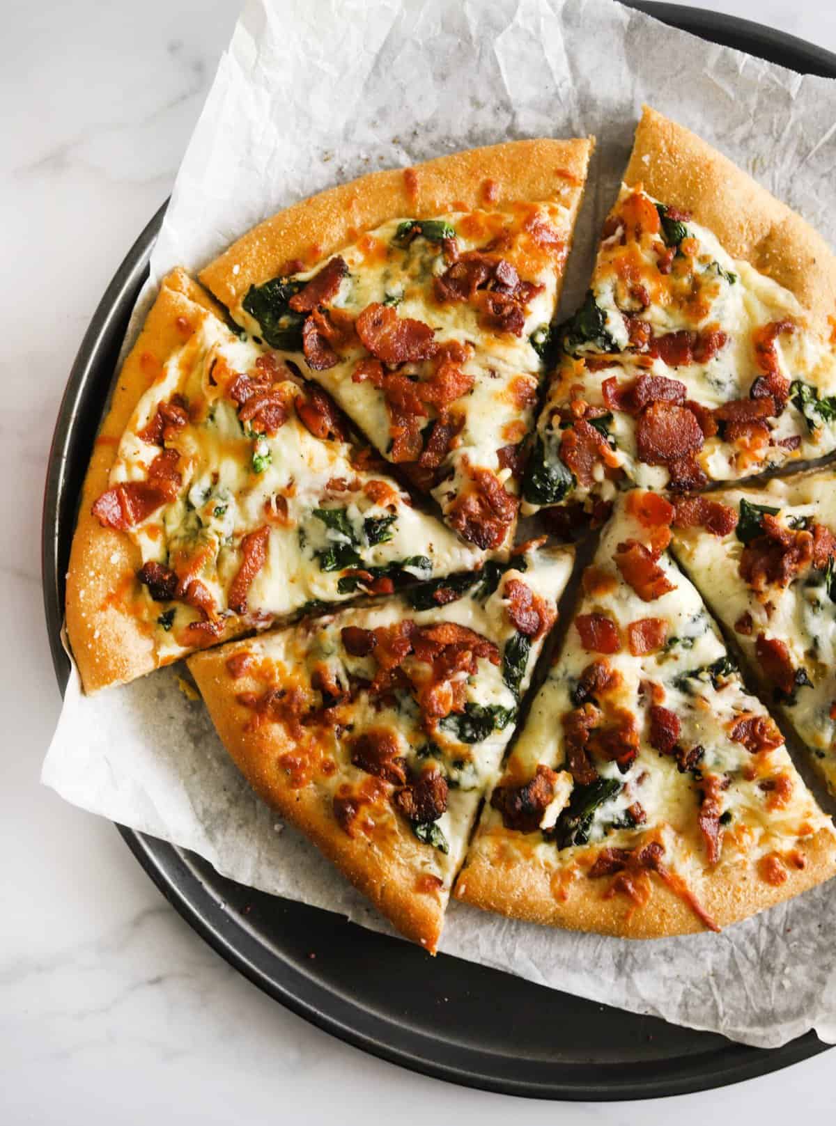 An overhead shot of slices of white pizza with bacon and spinach.