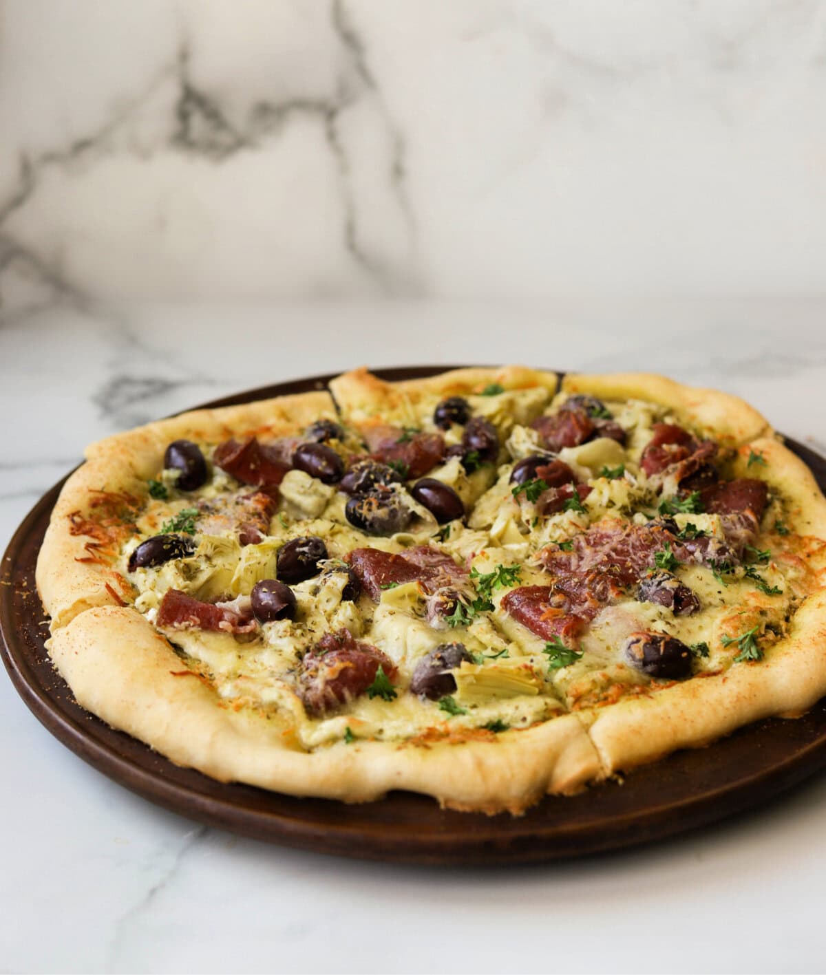 A front shot of an antipasto pizza on a pizza stone.