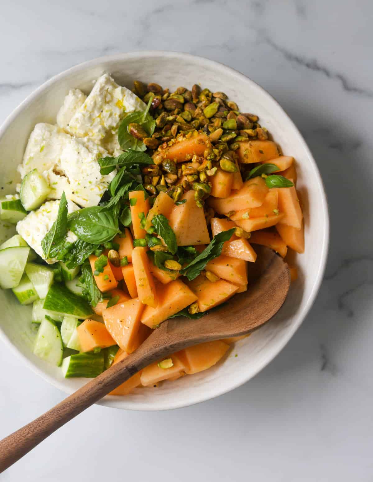 An overhead shot of a bowl filled with cantaloupe and cucumber salad.
