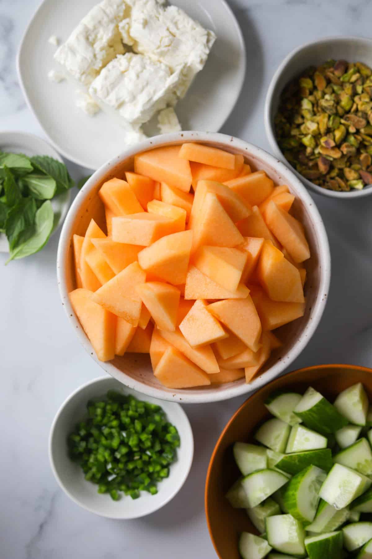 An overhead shot of bowls filled with ingredients for cantaloupe salad.