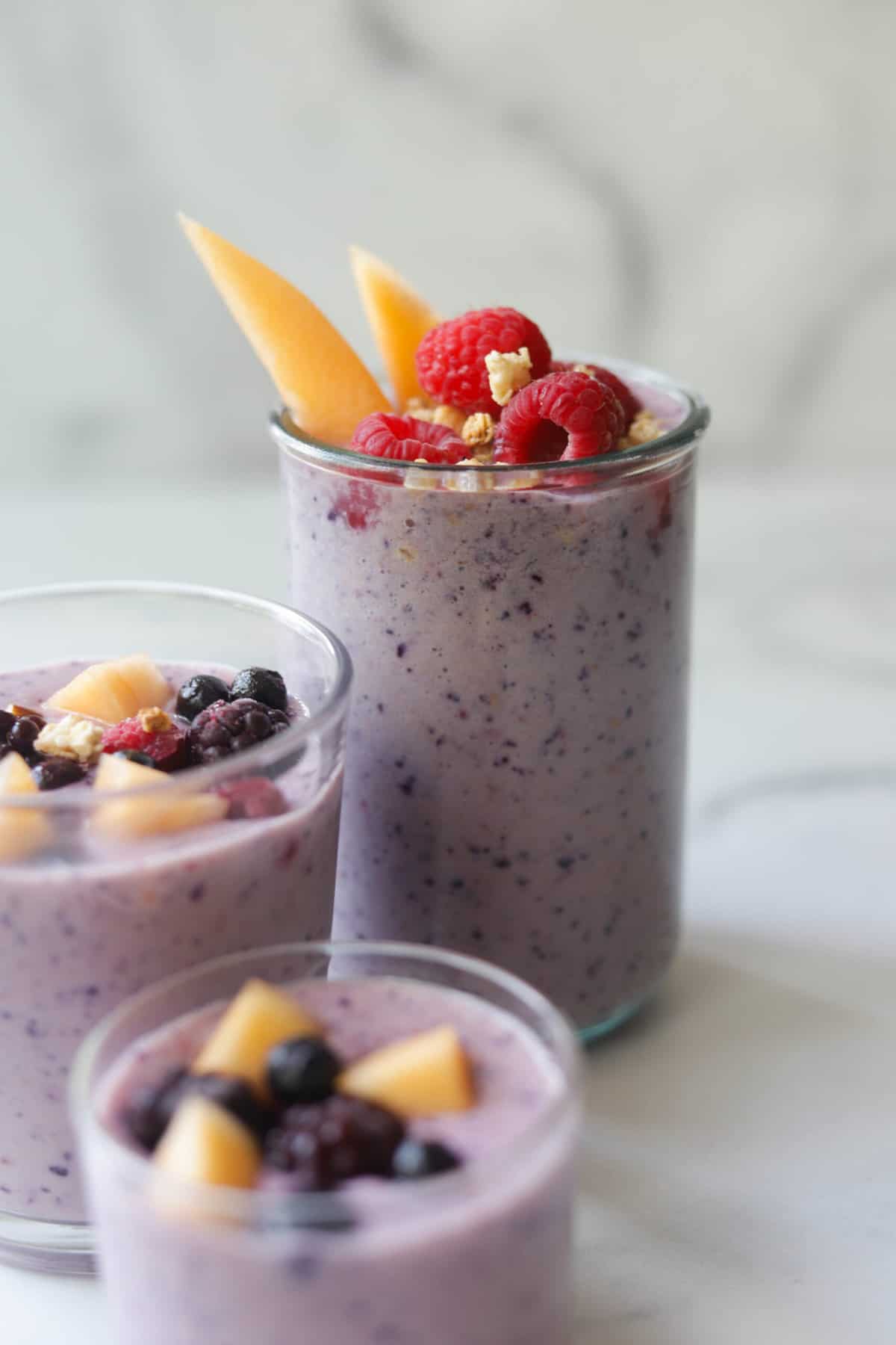 Three smoothie cups with fruit on top.