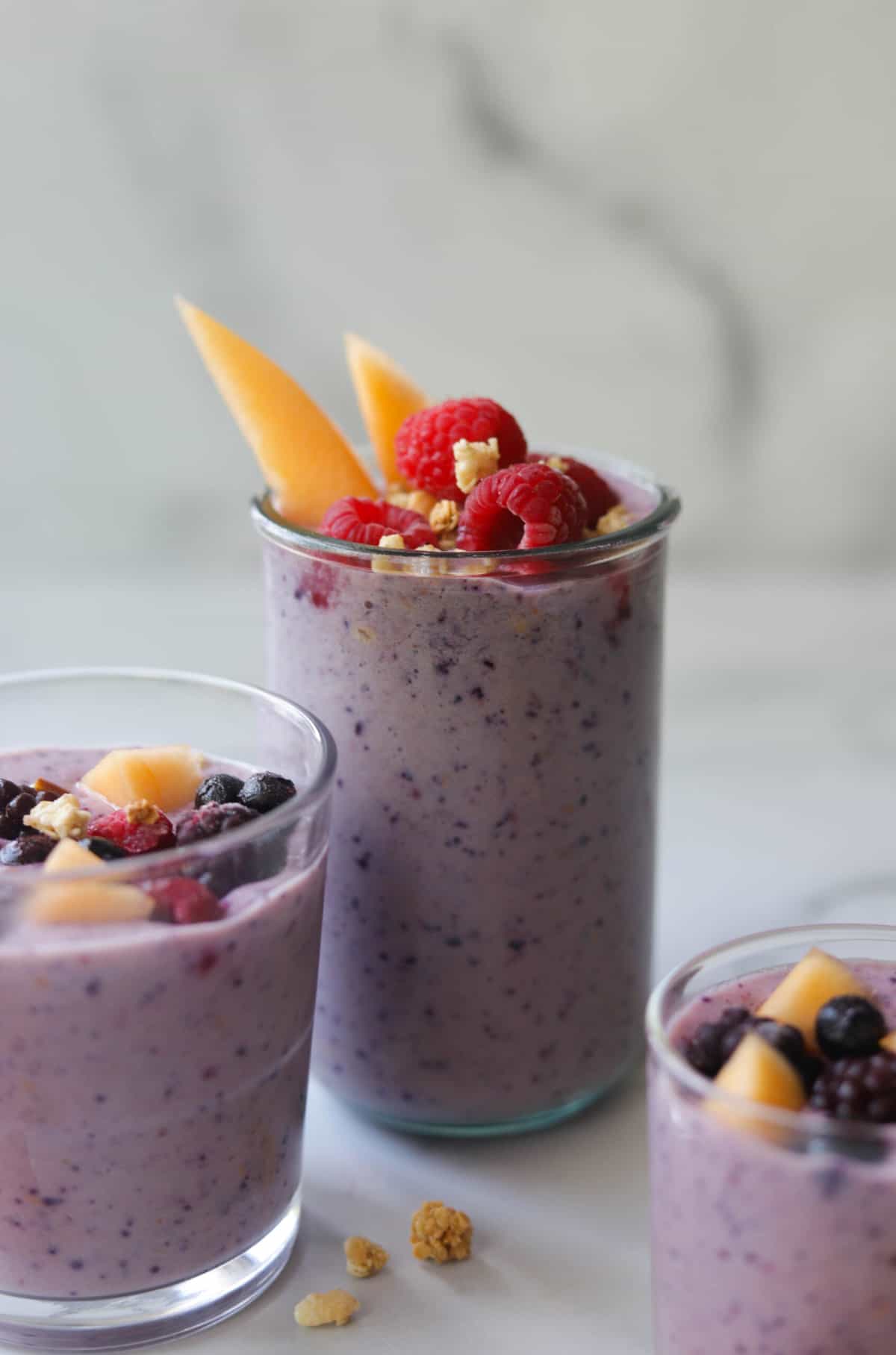 A front shot of glasses of berry cantaloupe smoothie with berries and cantaloupe garnished on top.