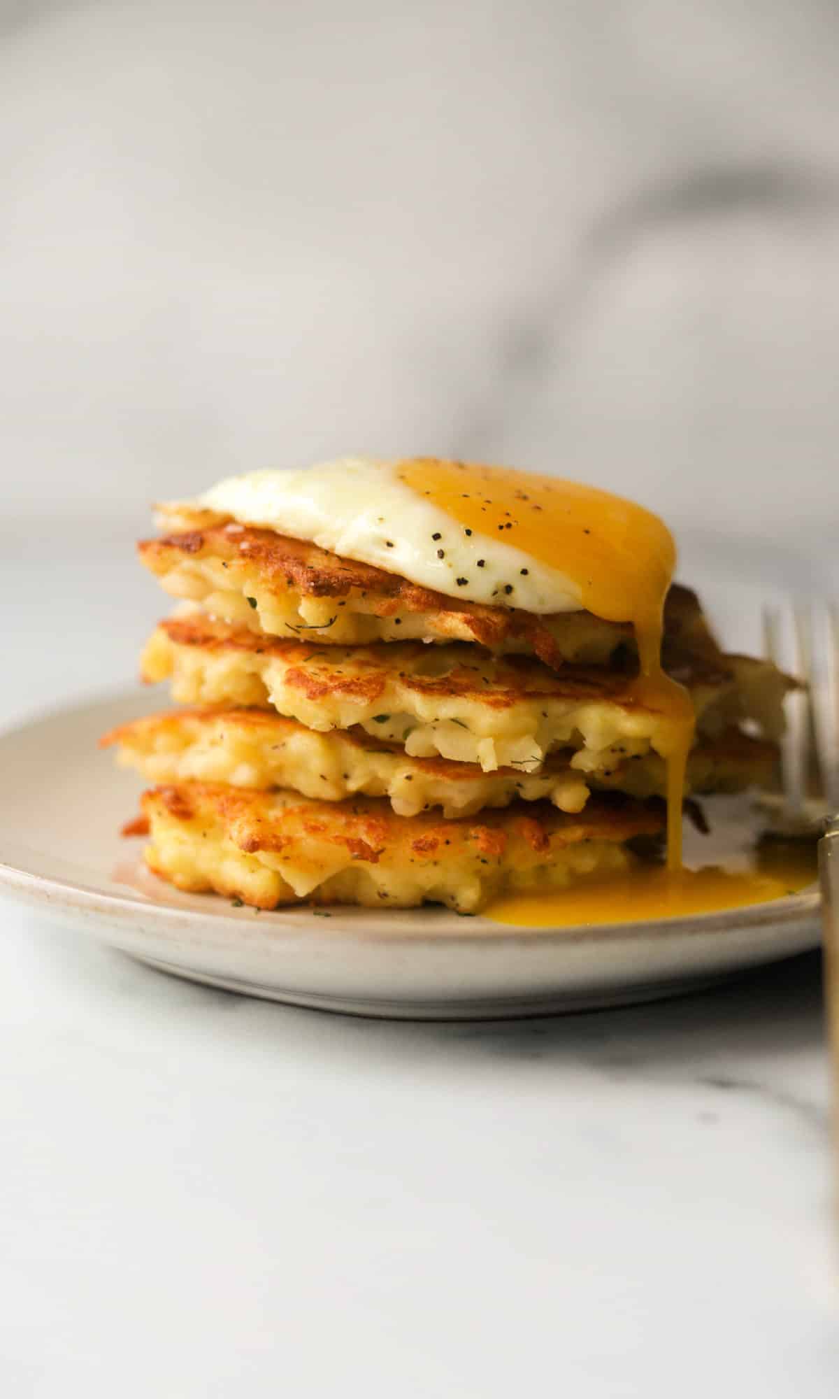 A side shot of a stack of crispy hash brown patties with a runny egg on top.