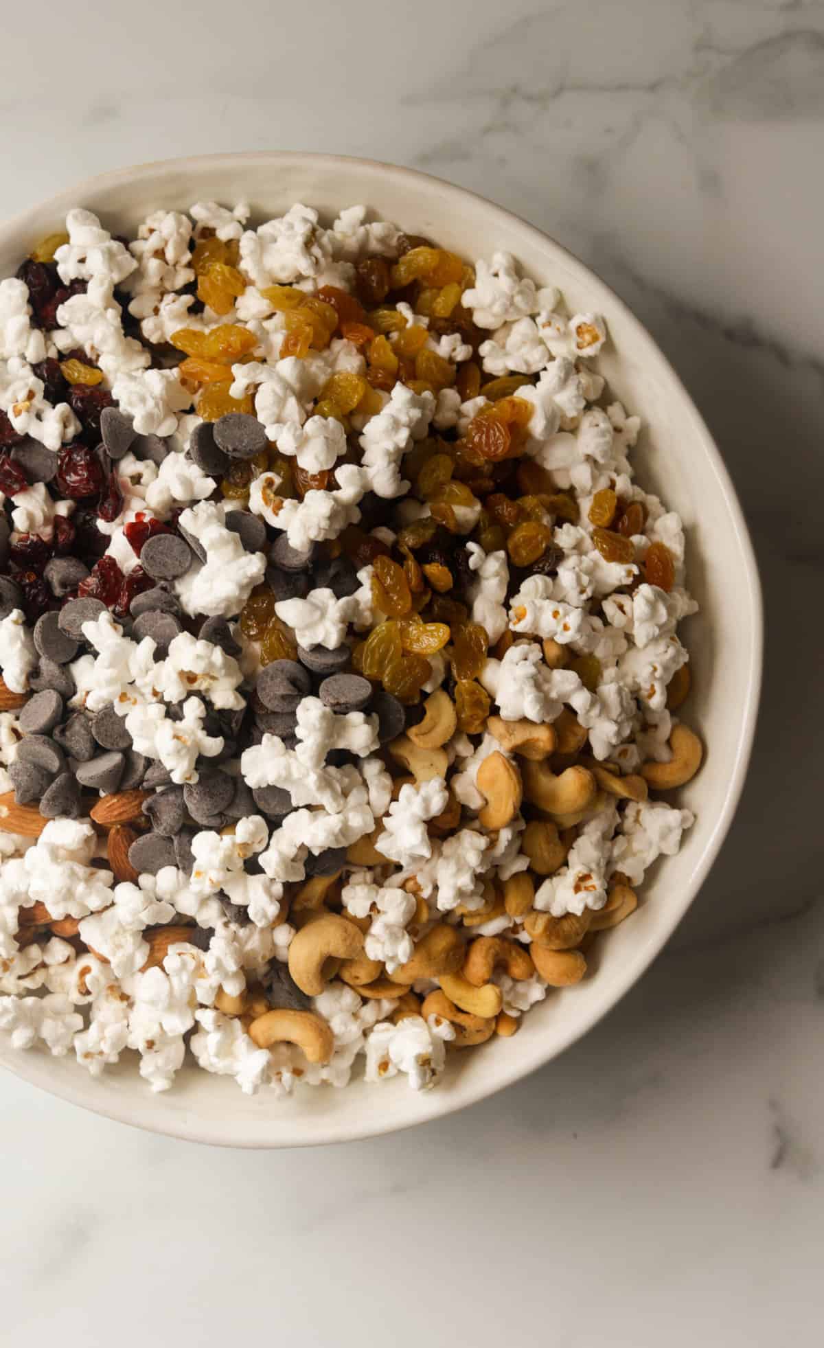 An overhead shot of a white bowl filled with popcorn trail mix.