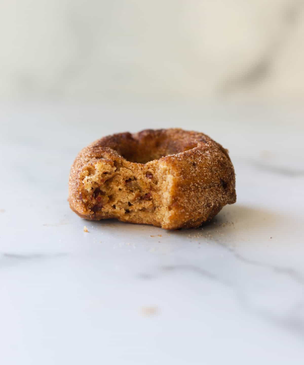 A side shot of a single apple date donut with a bite taken out of it.