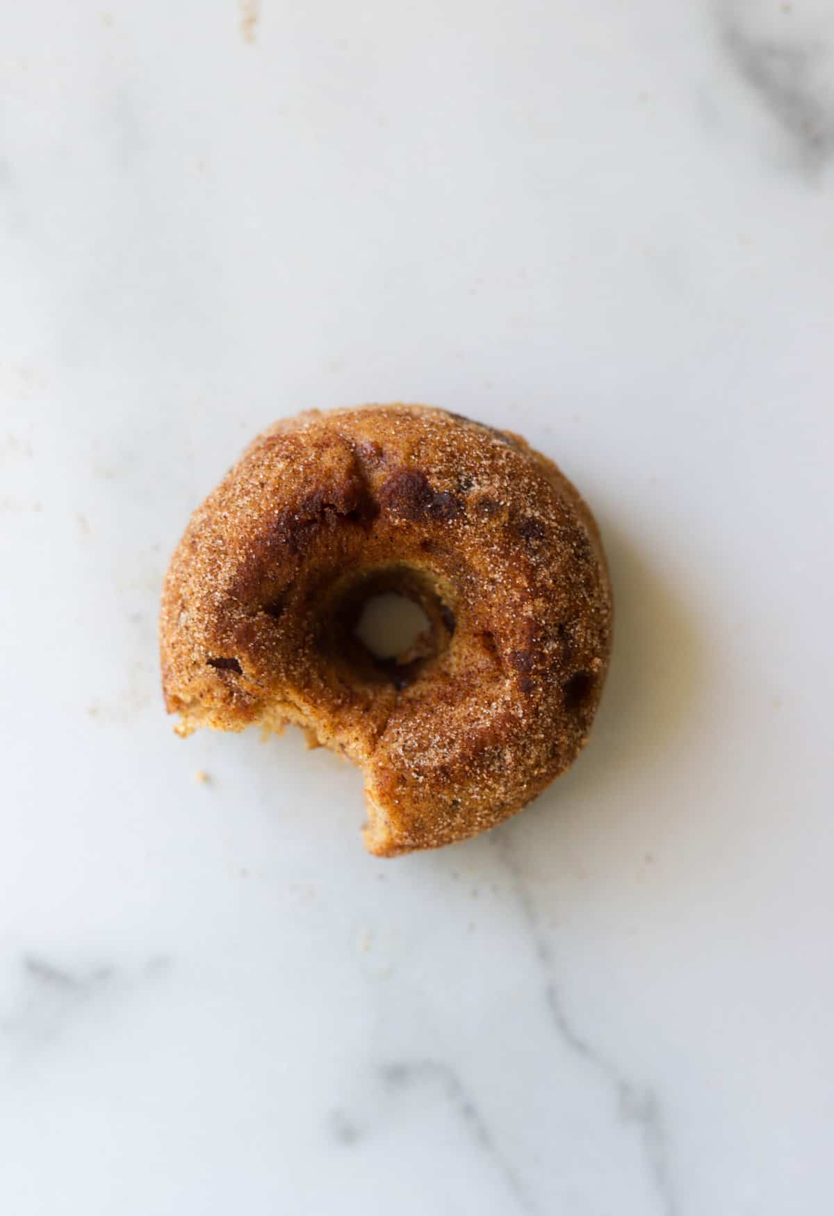 An overhead shot of a single apple date donut with a bite missing.