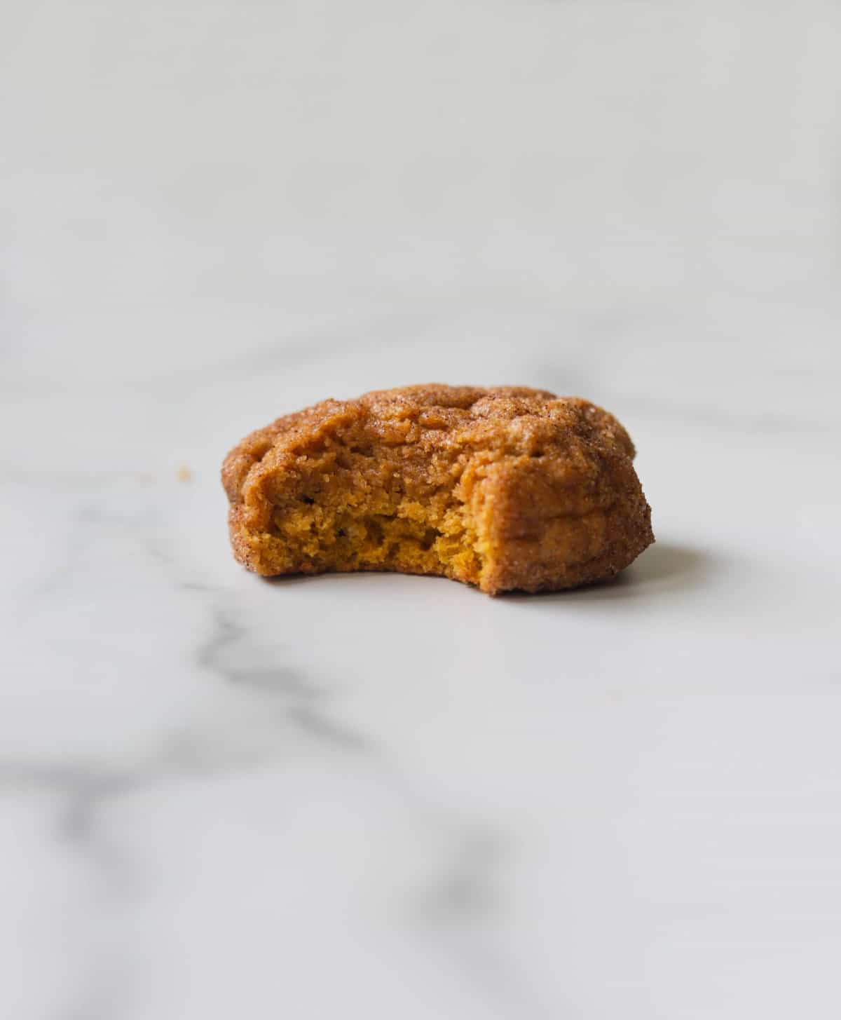 A side shot of a single pumpkin cookie with a bite missing.