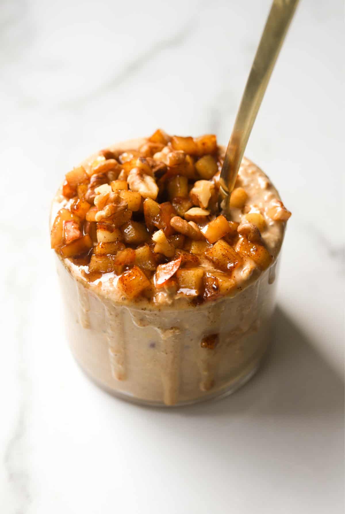 A side shot of a jar of apple pie overnight oats with a spoon coming out of it.
