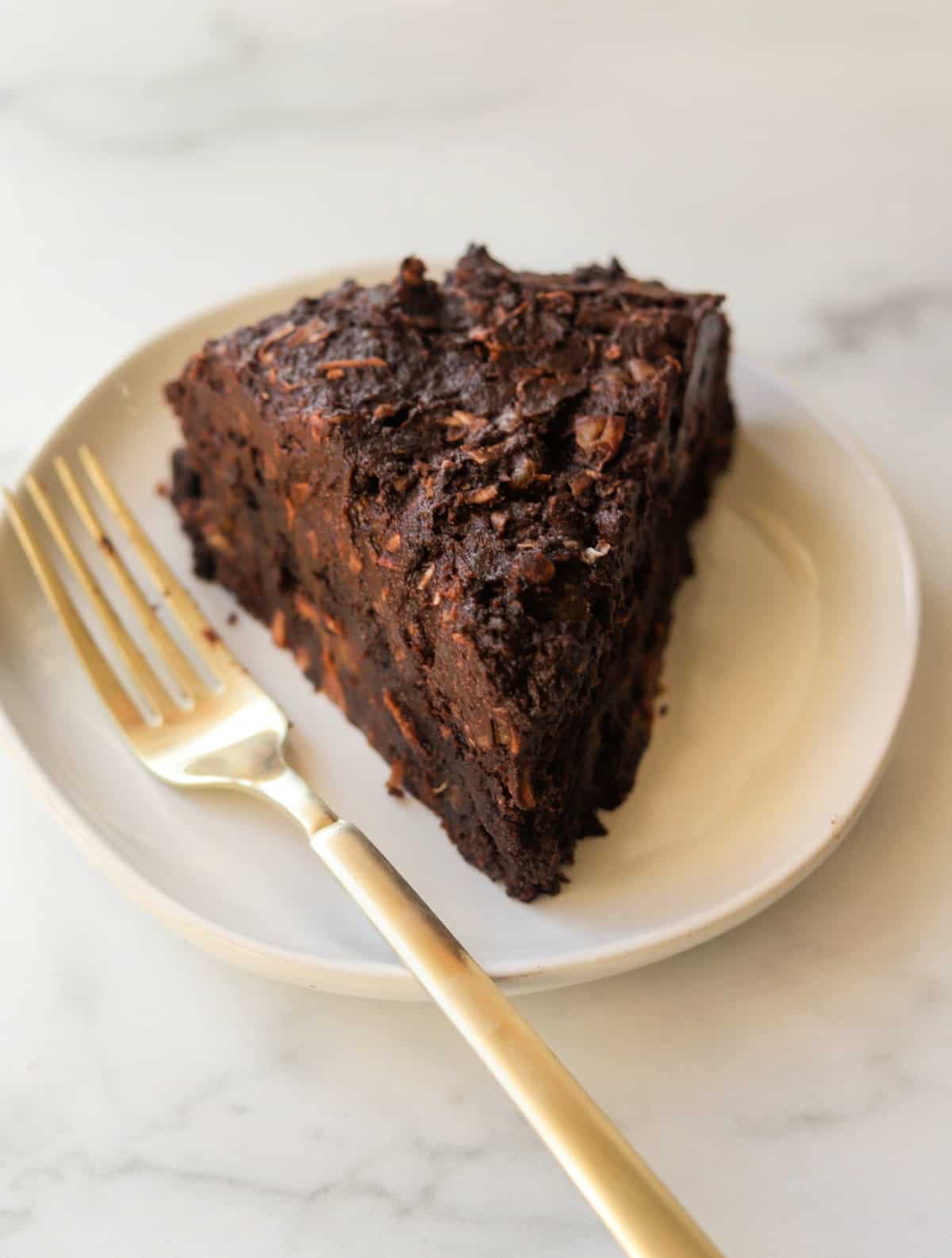 A side shot of a slice of dark chocolate date cake on a white plate.