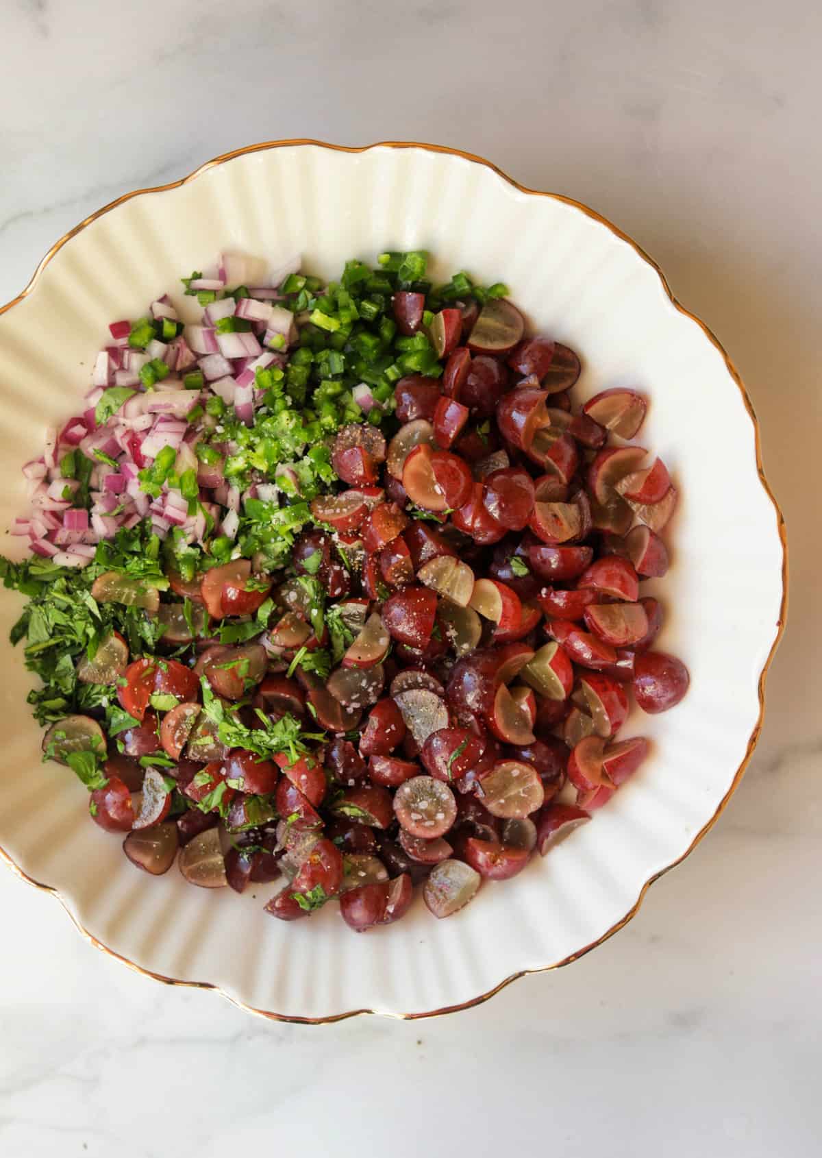 An overhead shot of a bowl of grape salsa ingredients.