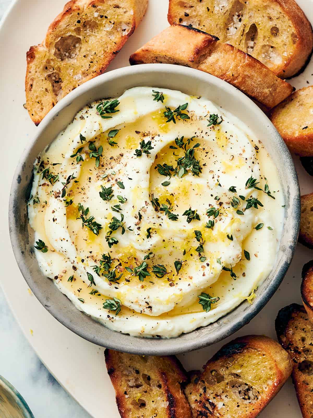 An overhead shot of a bowl of whipped ricotta dip and crostinis.