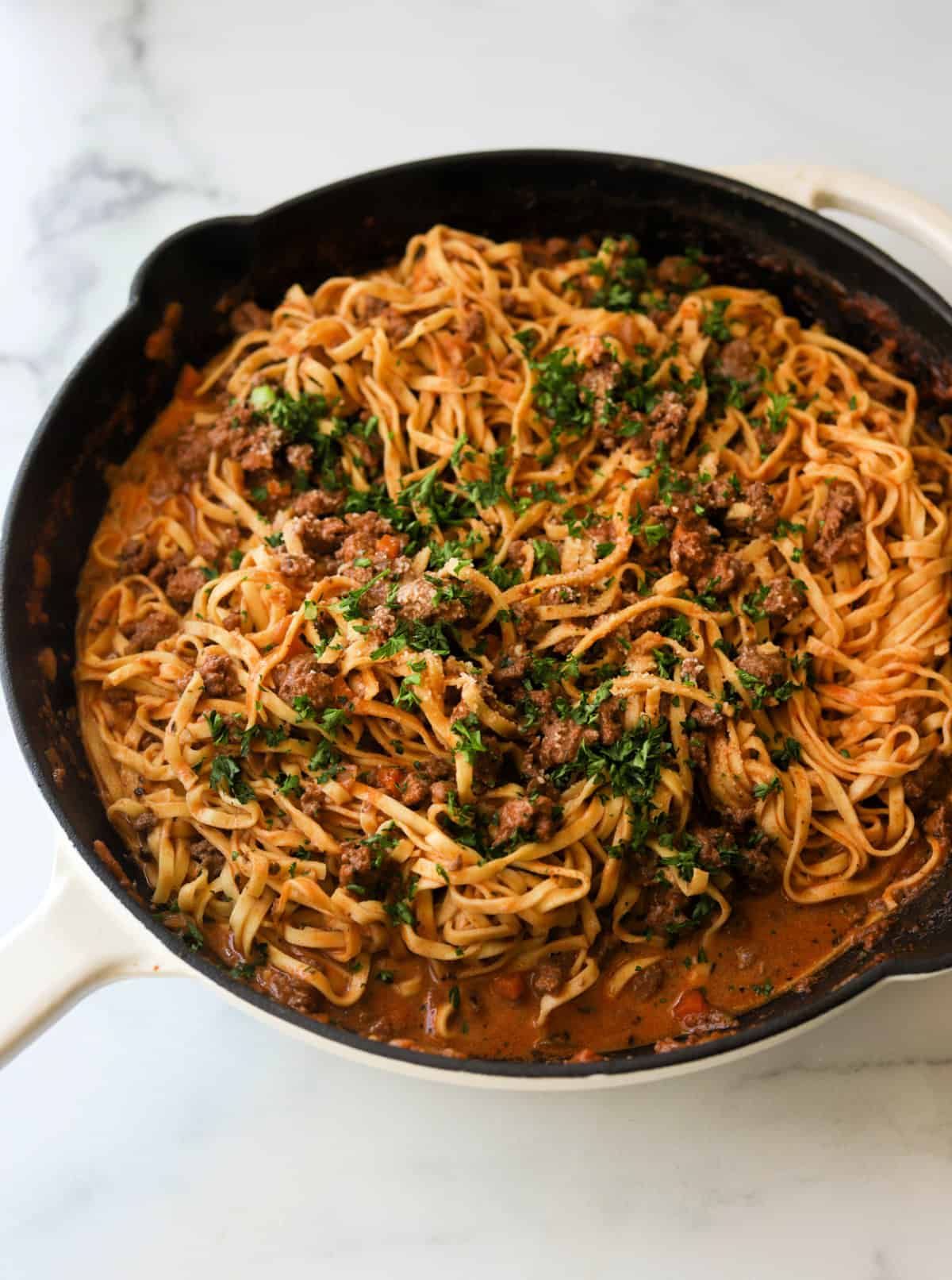 An angled shot of a skillet filled with linguine bolognese.
