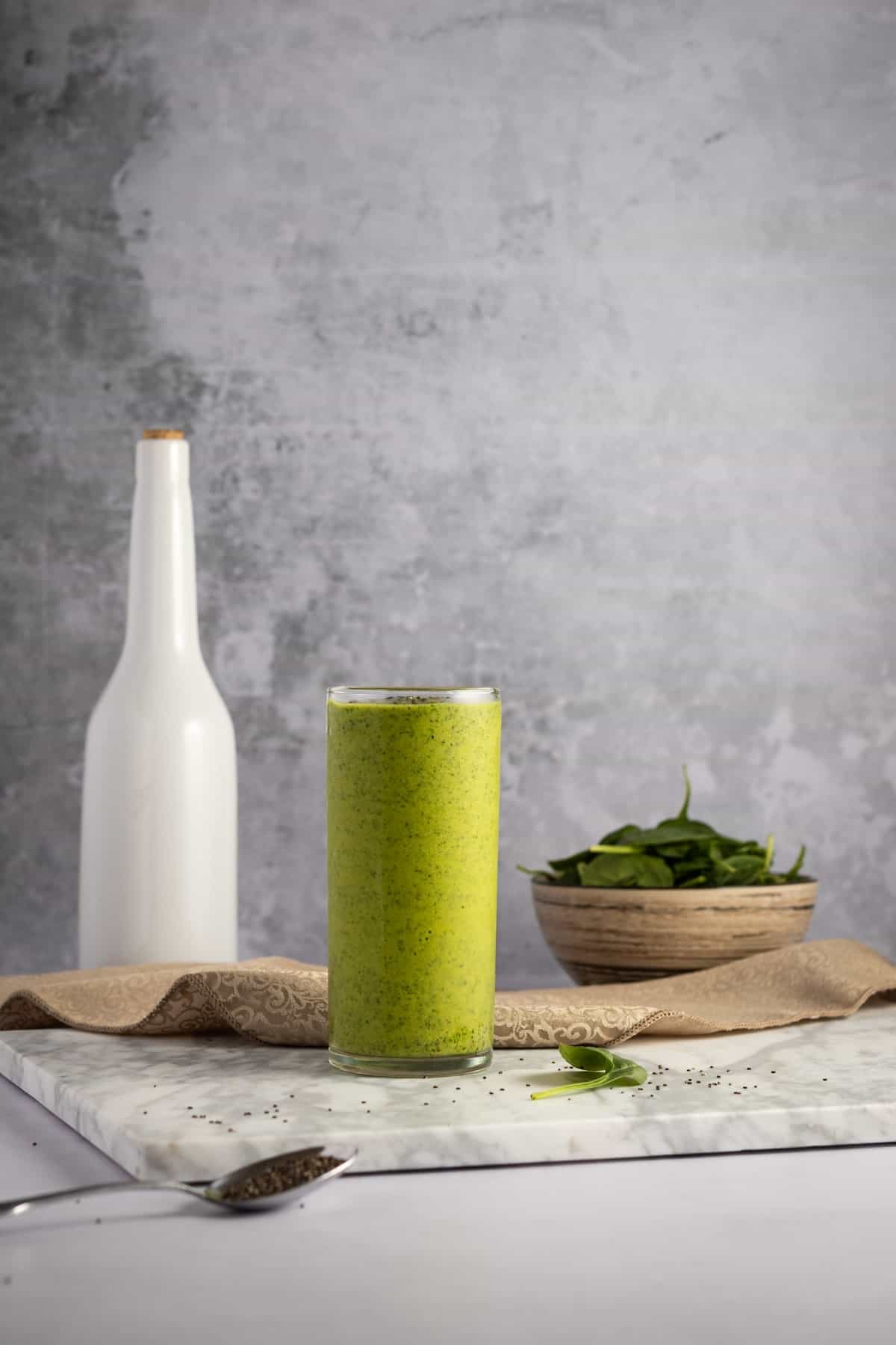 A side shot of a green smoothie with spinach and a bottle in the backdrop.